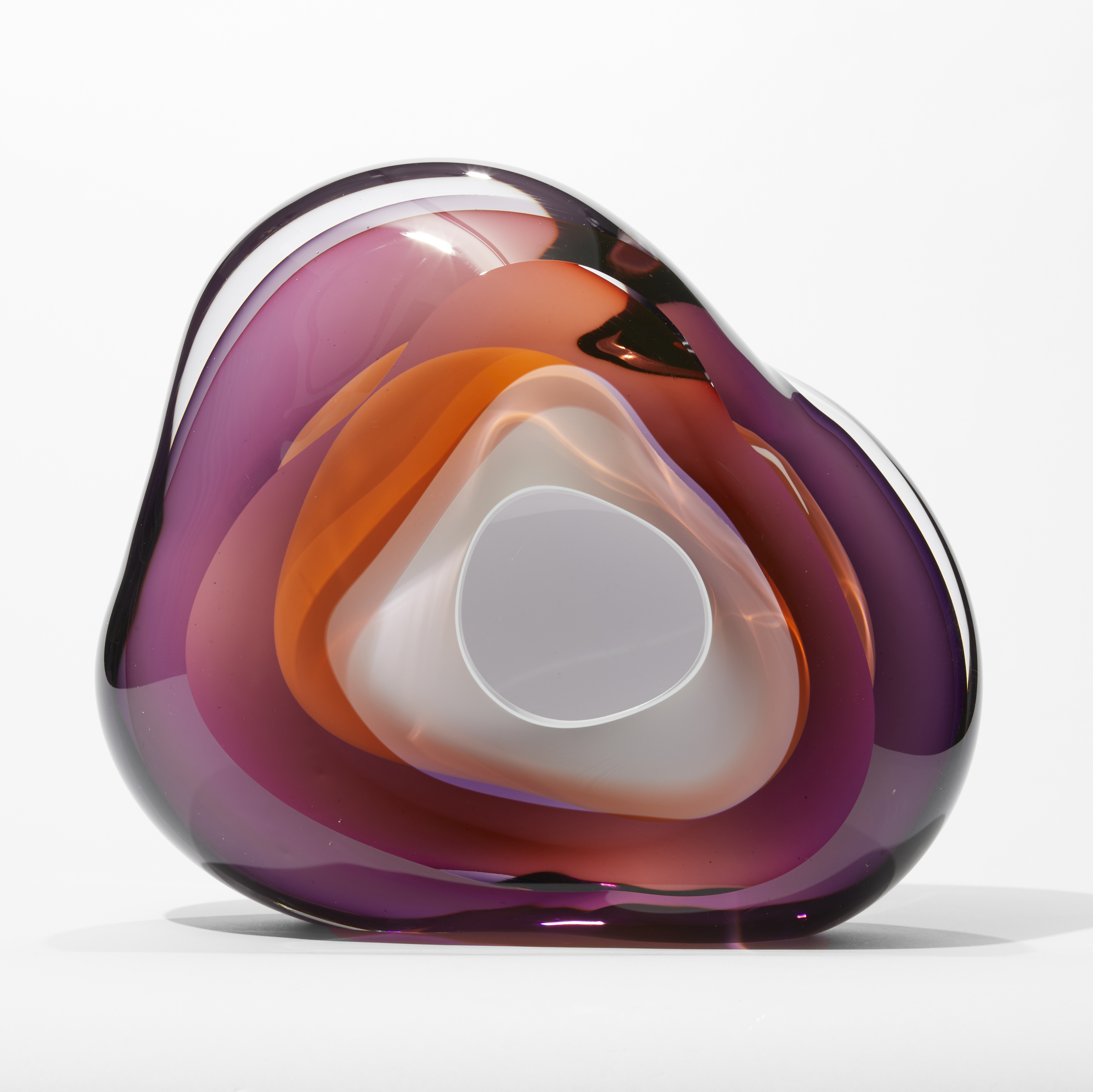 transparent soft amorphous rounded rock and geode inspired sculpture with a small front opening in layers of purple and orange with a central bubble of opaque white hand made from blown glass