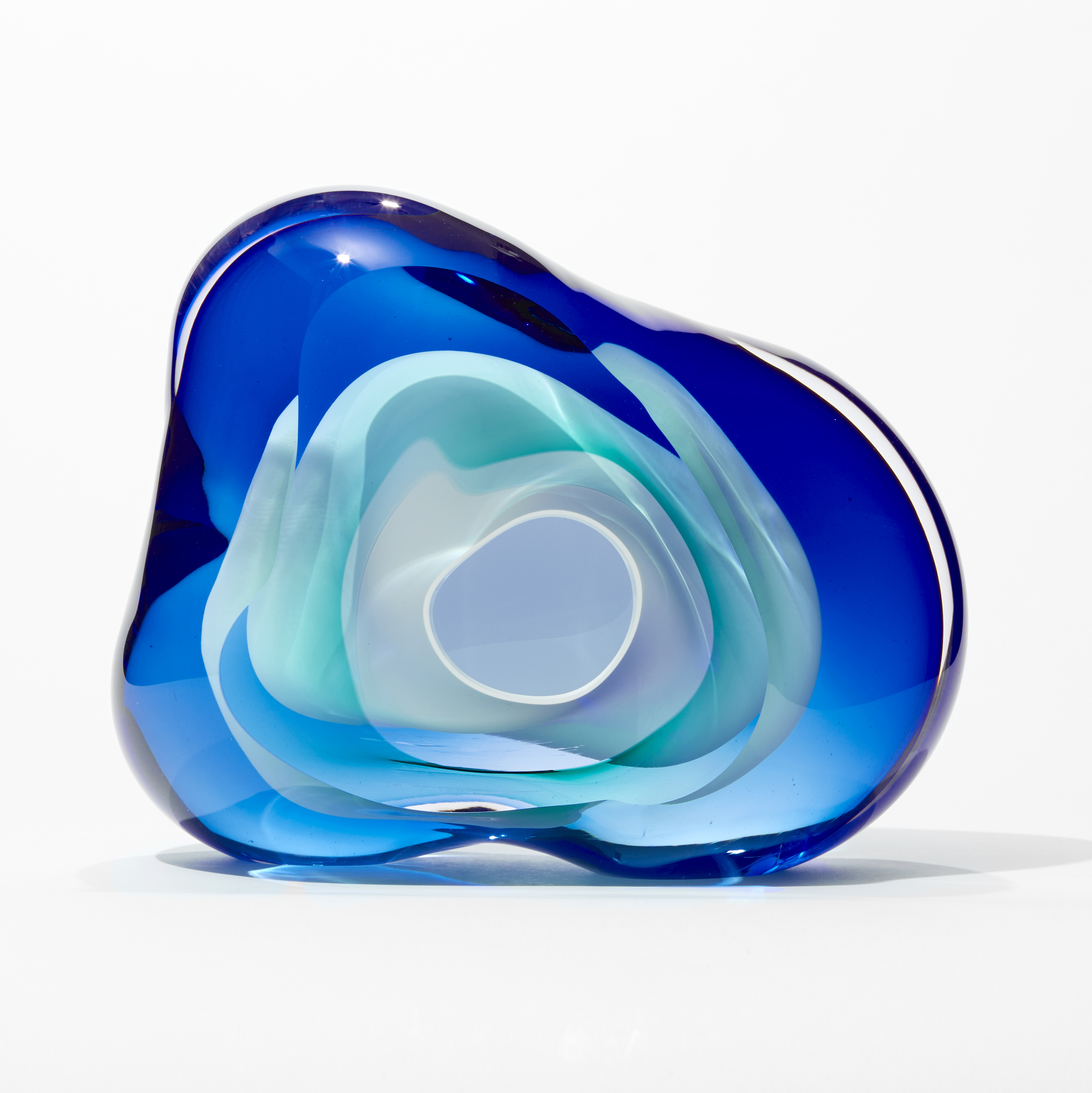 soft transparent amorphous organic rock inspired sculpture with front aperture opening in layers of clear intense blue and turquoise with a central cavity lined in opaque white hand made from glass
