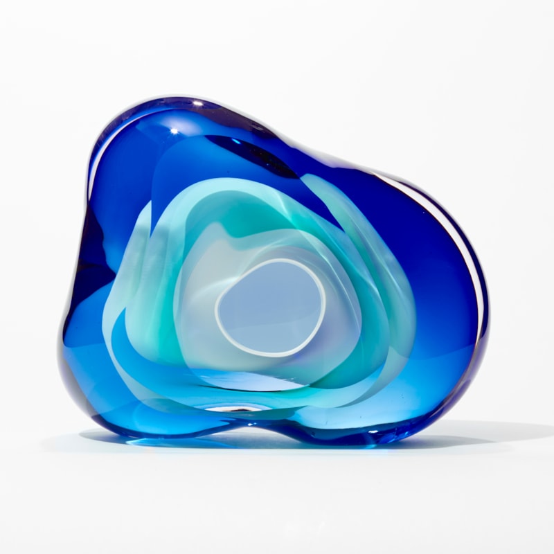 soft transparent amorphous organic rock inspired sculpture with front aperture opening in layers of clear intense blue and turquoise with a central cavity lined in opaque white hand made from glass
