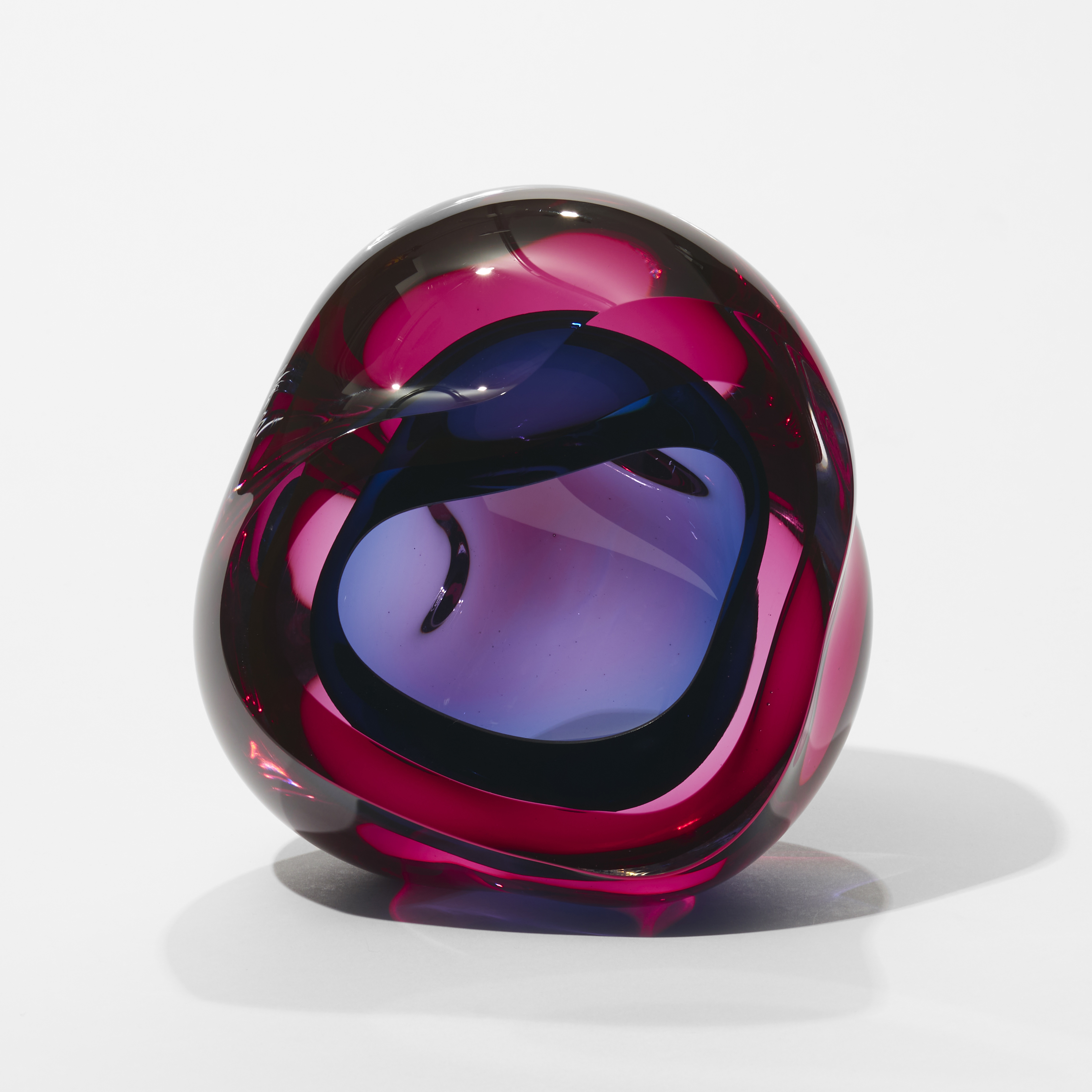 transparent pink and indigo blue geode inspired sculpture with a soft undulated amorphous shape and central cavity and front facing opening hand made from glass