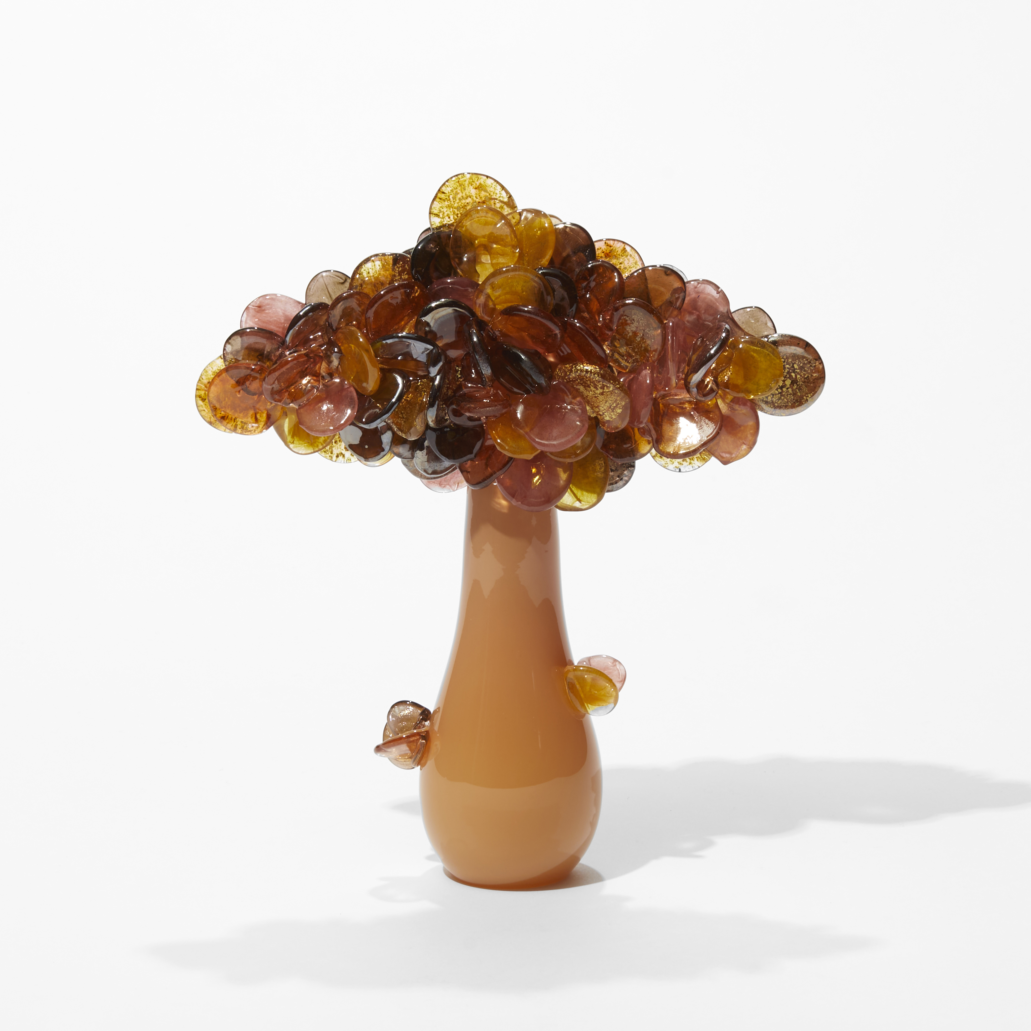 short tree sculpture with a pear shaped trunk in opaque soft orange with a horizontal diamond cluster of round sugary colour leaves in amber aubergine and pink with flecks of gold hand made from blown glass