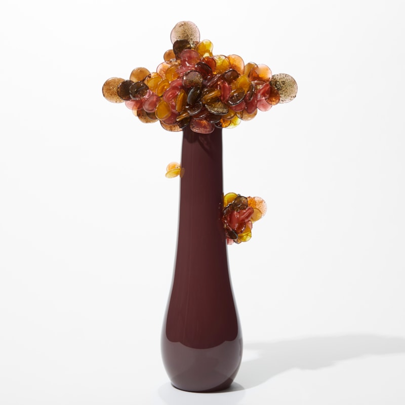 tree inspired artwork with a long sleek shiny trunk in aubergine and a cluster of round leaves perched on the top in brown pink amber and bronze with gold leaf speckles hand made from glass