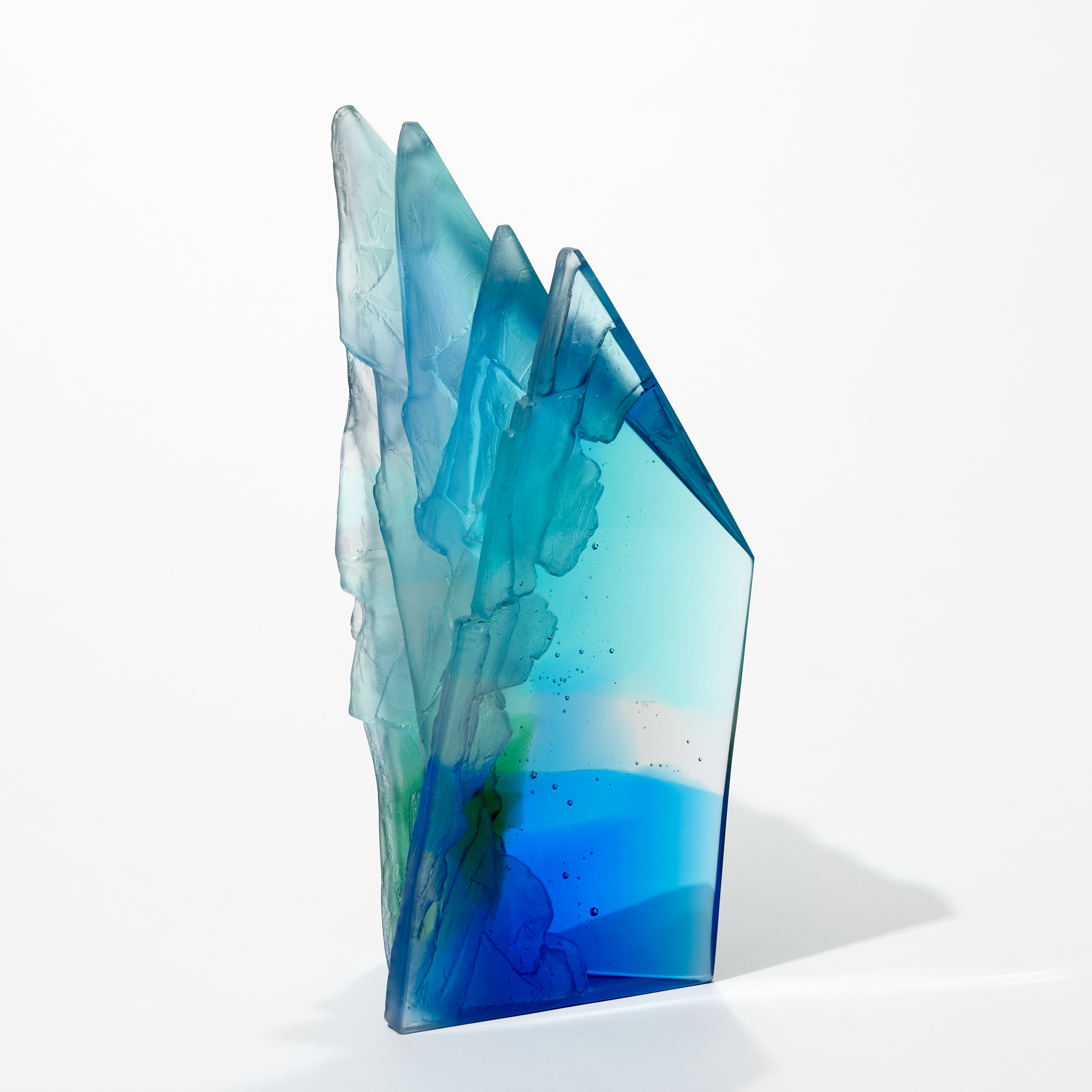 graphic geometric tall rhombus standing cliff inspired sculpture in transparent blue green aquamarine and turquoise with two flat shiny sides and two highly textured sides hand made from cast glass