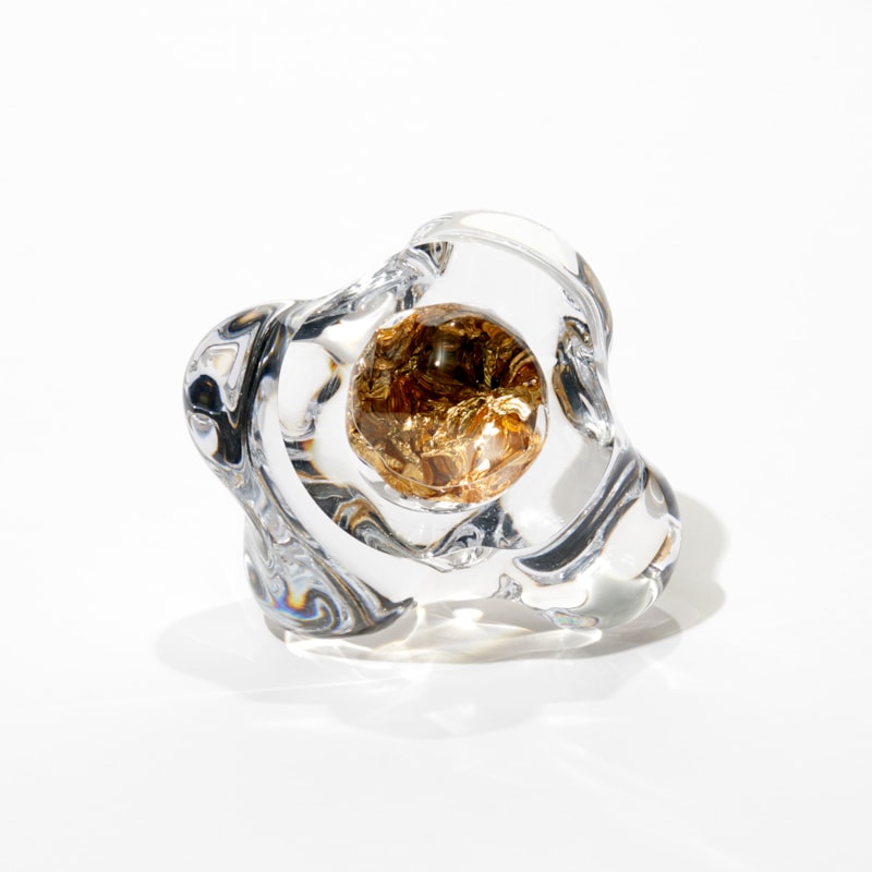 amorphous sculpture resembling a piece of rounded crystal clear ice with a central encased hole filled with crushed gold leaf hand blown and cut from glass