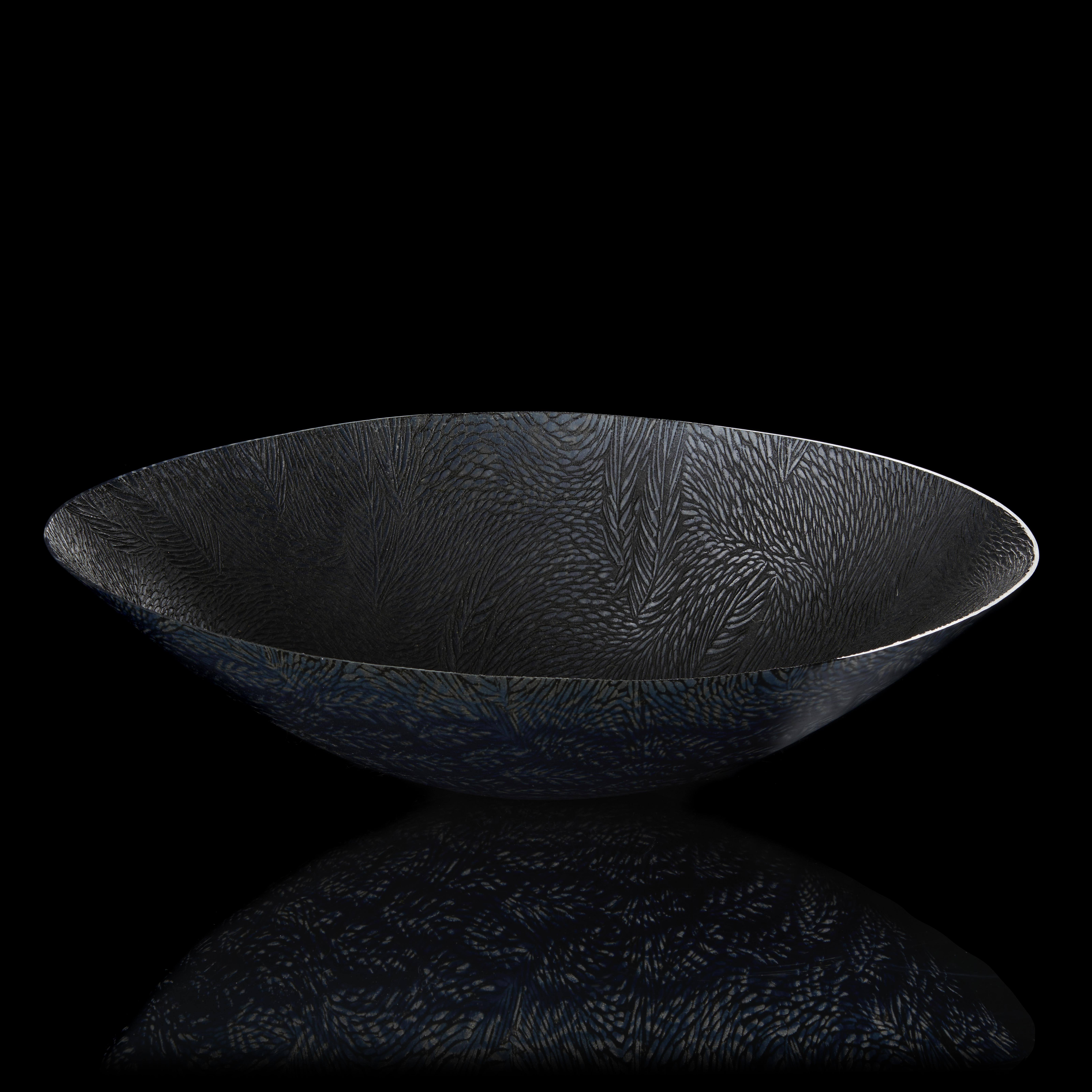 translucent black light grey and dark blue oval bowl perched on a small rounded base with sweeping sides and a fine organic texture moving over the surface resembling ears of corn hand made from glass