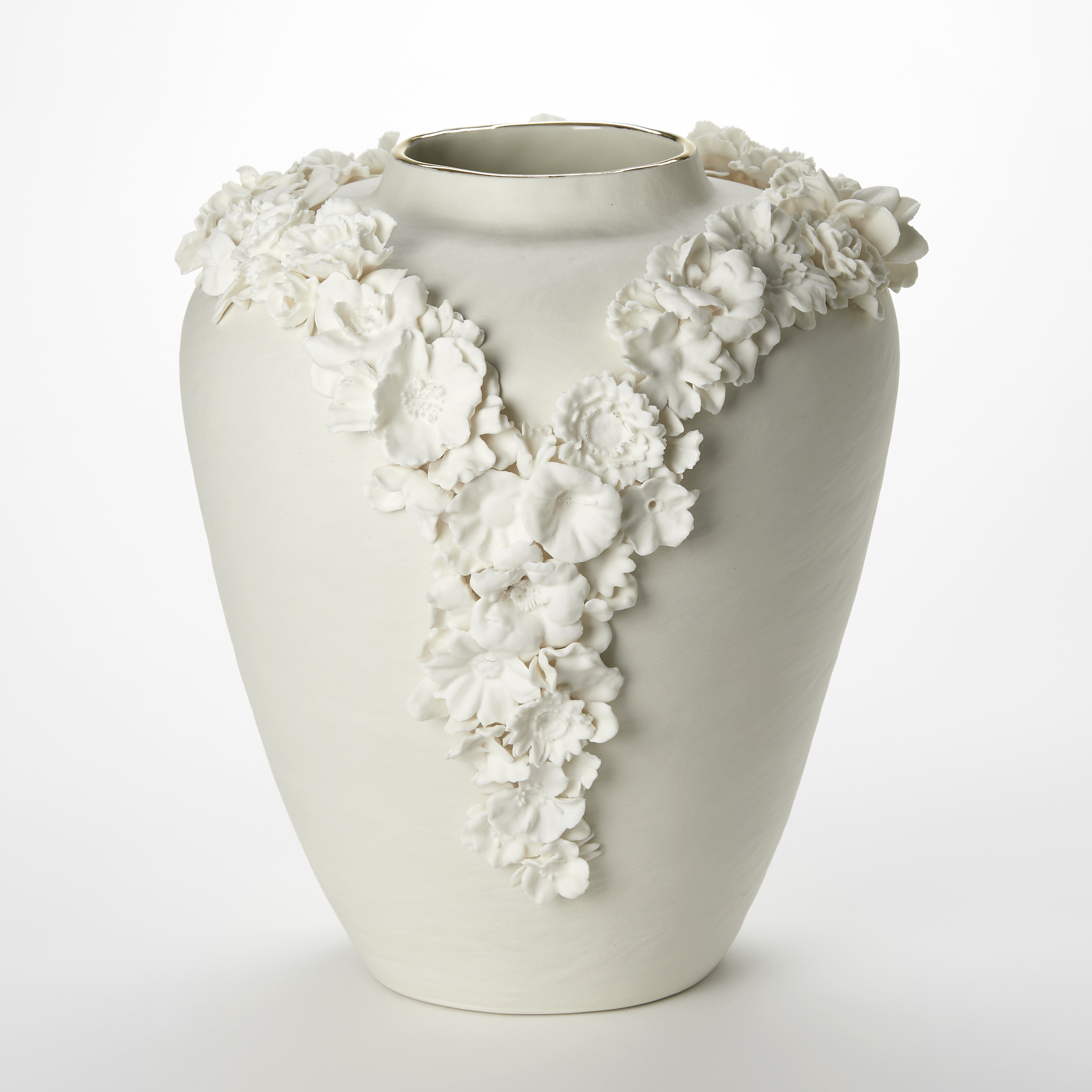 off white cream tall rounded vase with tapering base and narrowing top opening with a band of gold adorned with two lines of three dimensional flowers creating a v formation on the front like the plunging neck line of a ladies dress hand made from porcelain 