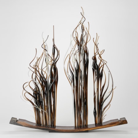 curved slice of oak from a barrel with three bunched sections of straight thin canes with curling ends in amber brown and clear protruding from the top edge and thrusting upwards with each hand made from glass