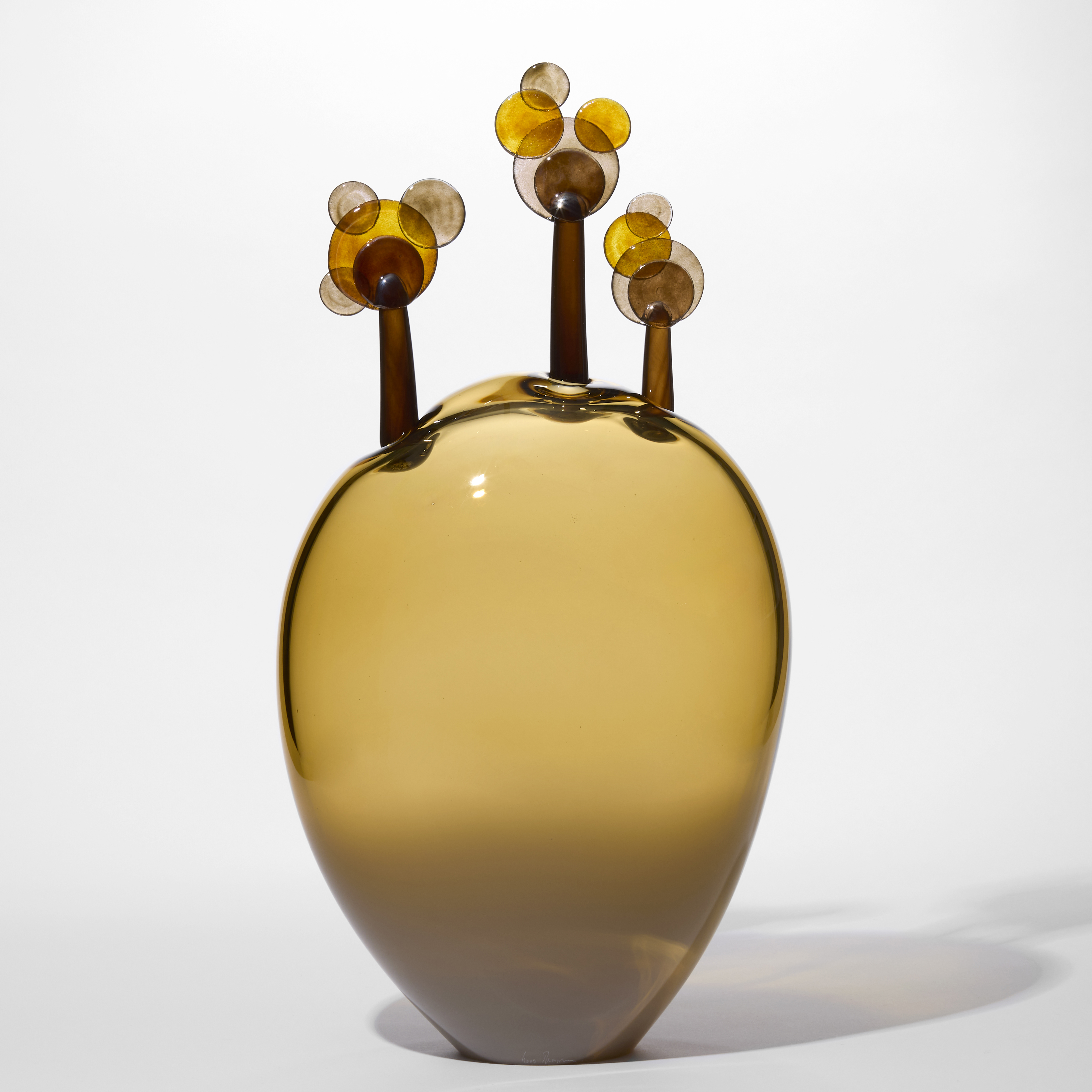 transparent inverted teardrop shaped olive green large standing form with three simplified lollipop trees perched on the rounded top in brown and amber all hand made from blown glass