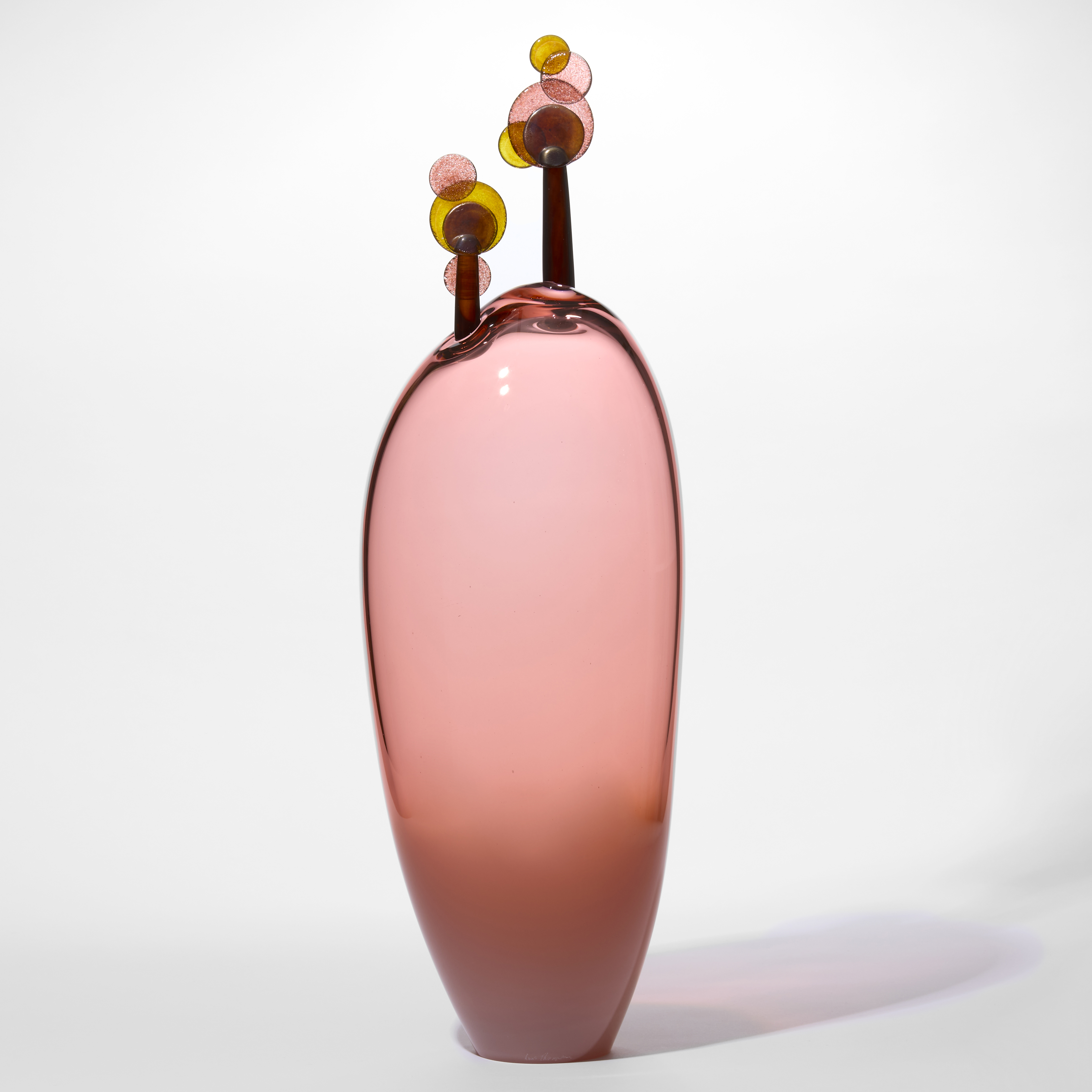 soft transparent peachy pink tall amorphic shaped form with two simplified lollipop trees perched on the rounded top with rounded leaves in brown amber and rose hand blown from glass