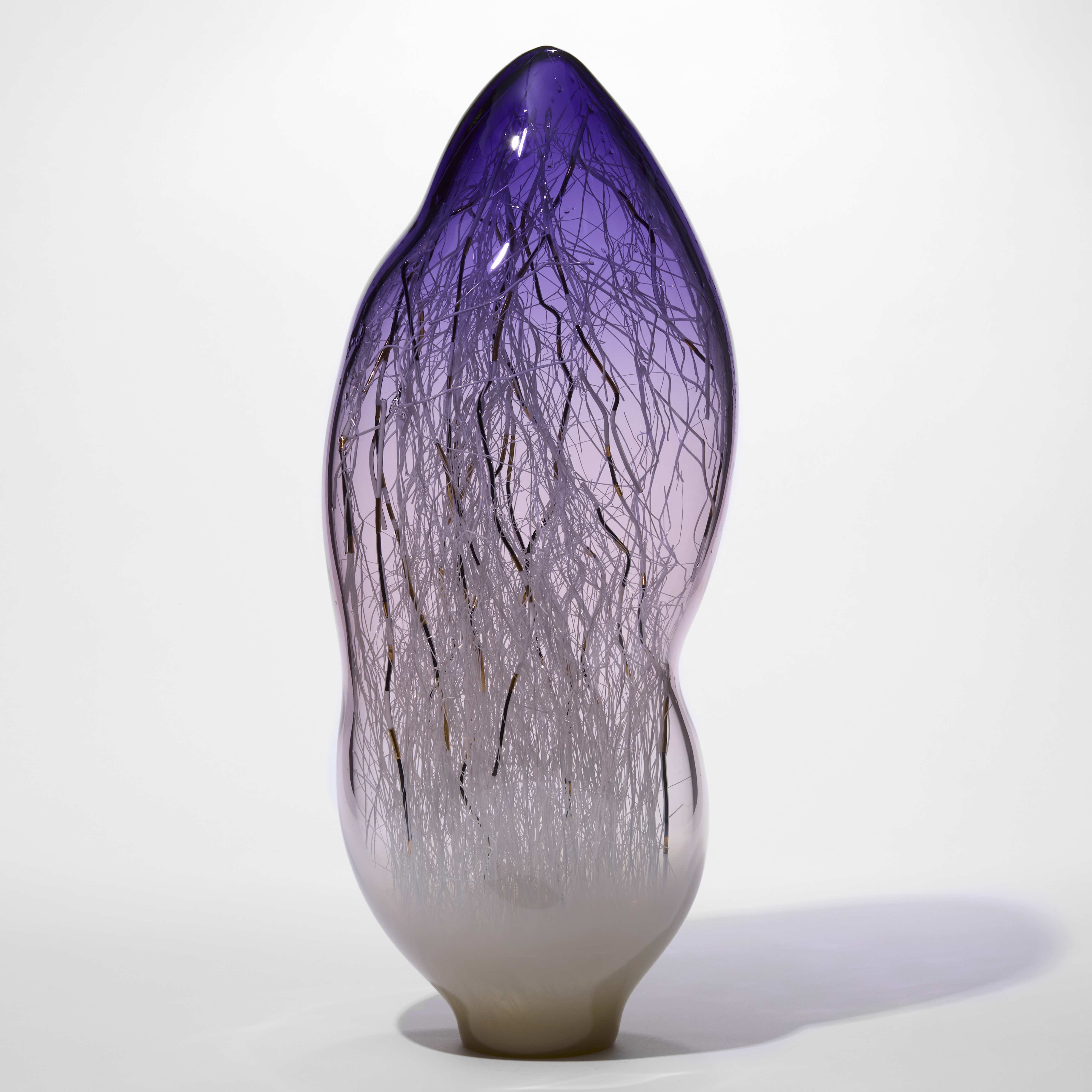 tall amorphic sculpture in transparent purple fading at the bottom and turning to milky opaque white with fine long canes in white black and gold trapped on the inside hand made from glass