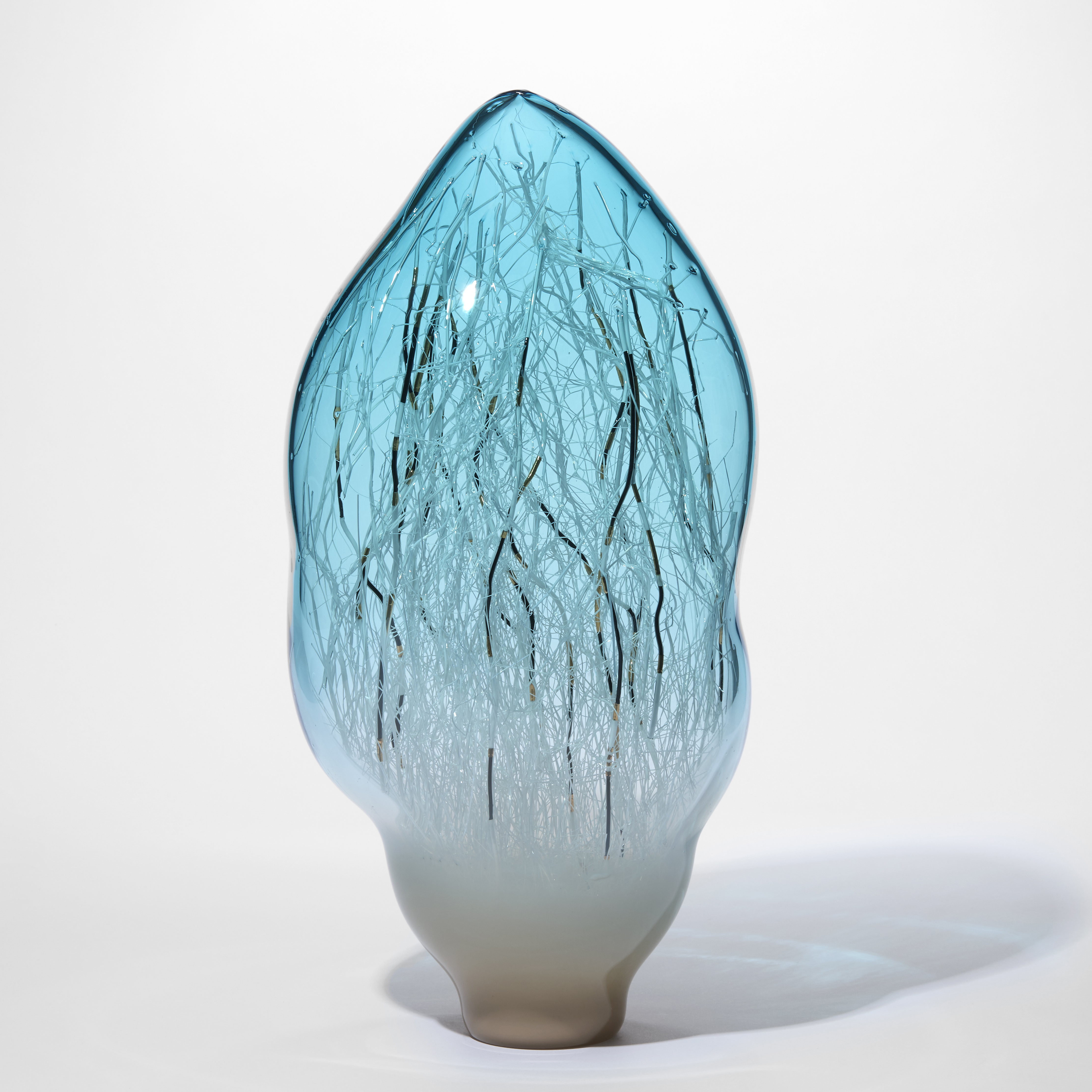 standing amorphic sculpture in transparent aquamarine fading towards the base turning to milky warm white with the internal filled with fine canes in white black and gold made from hand blown glass