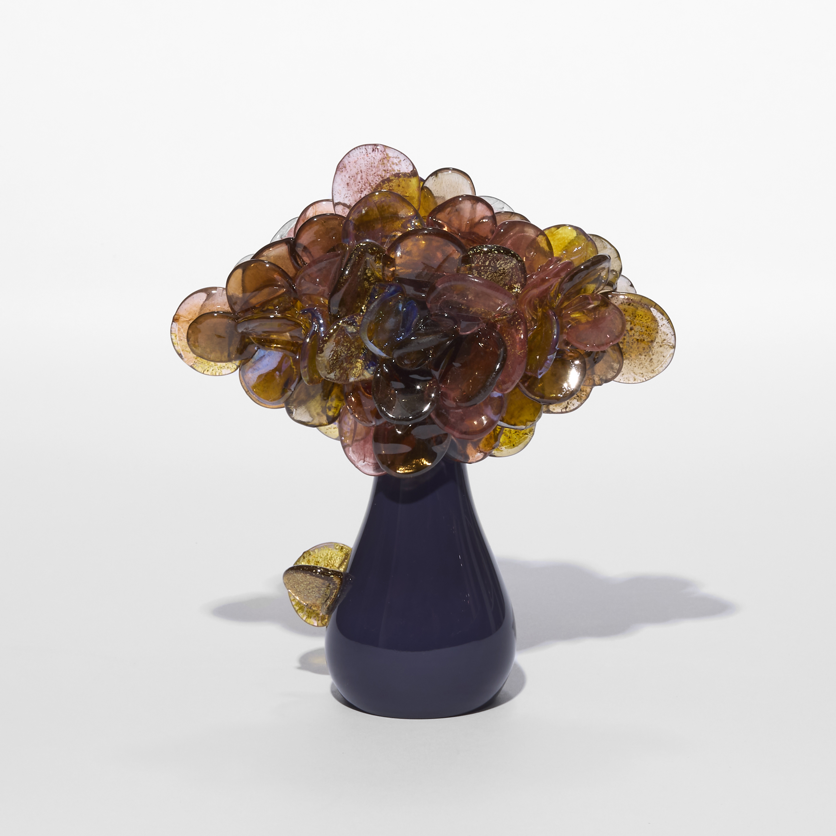 small cute simplified tree sculpture with a pear shaped glossy trunk in plum and a cluster of shiny lollipop round leaves clustered on the top in aubergine pink and amber with gold flecks trapped within each leaf hand made from blown glass
