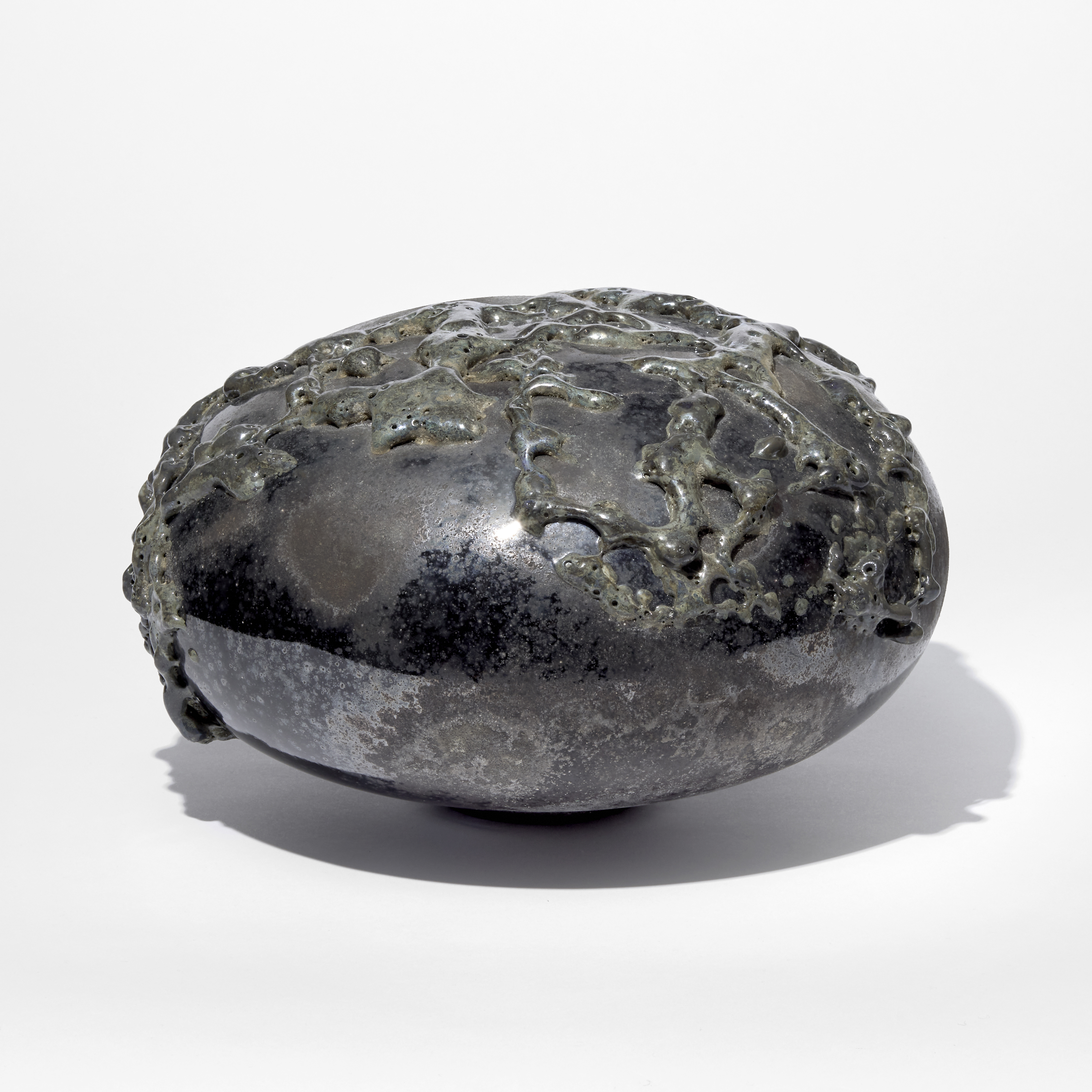 black rounded low mushroom shaped sculpture with leathery weathered surface covered in organic raised surface texture with a dark metallic sheen hand made from glass
