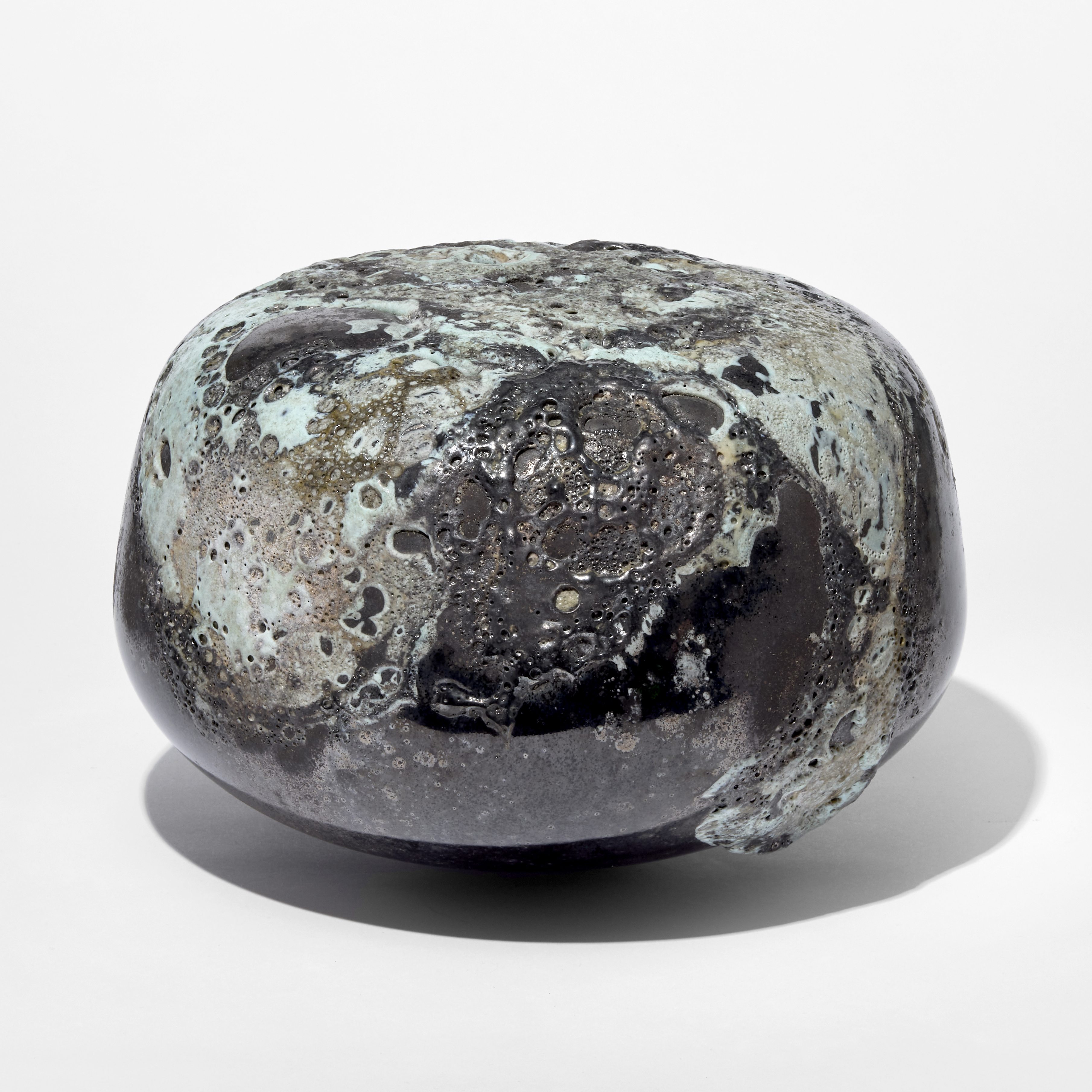low rounded squat dark pewter coloured pebble with raised matt organic pitted sections in soft jade green hand blown from glass