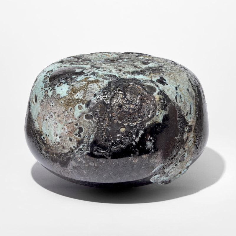 low rounded squat dark pewter coloured pebble with raised matt organic pitted sections in soft jade green hand blown from glass