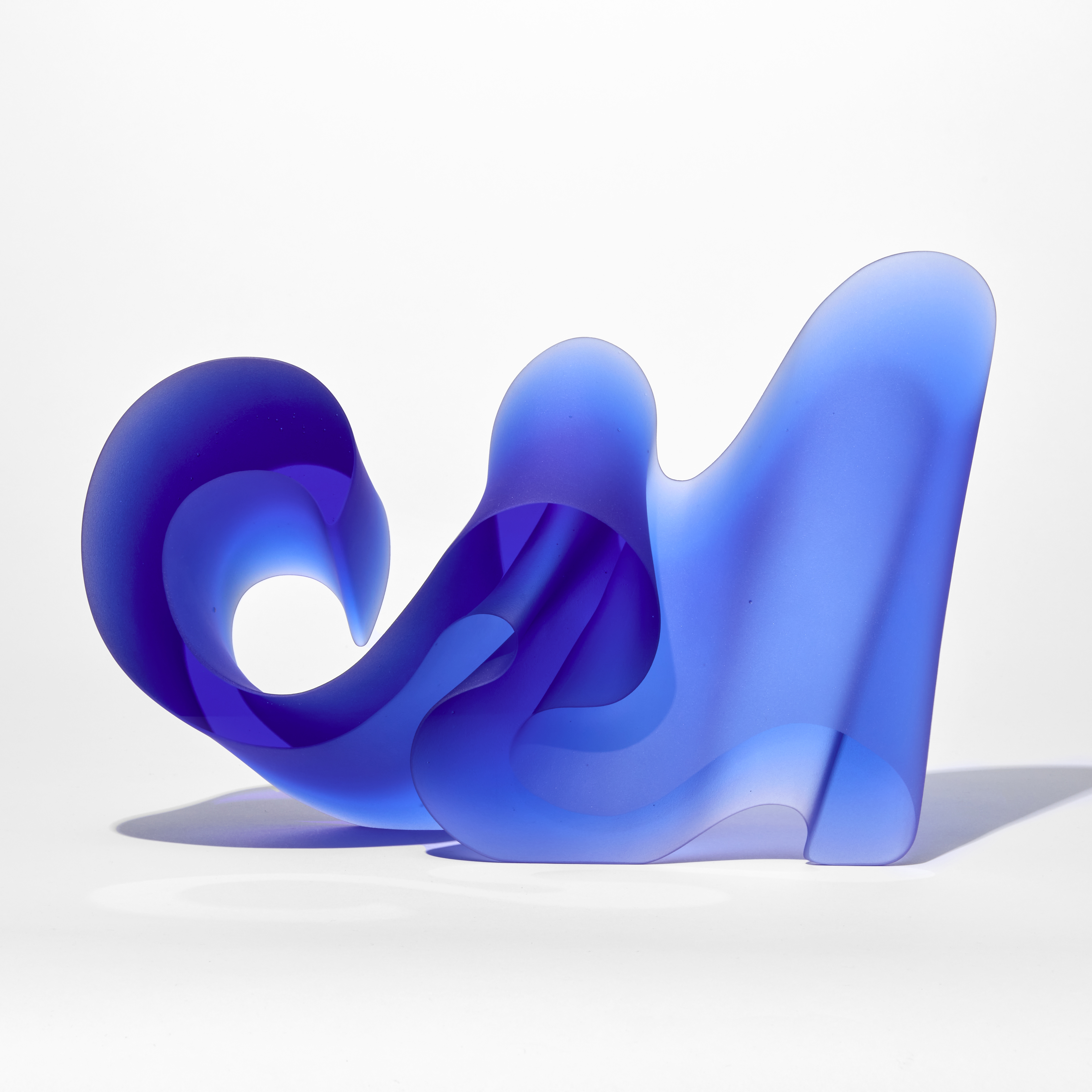 intense semi transparent blue prone curling and undulating standing form with a flat front and back hand made from glass