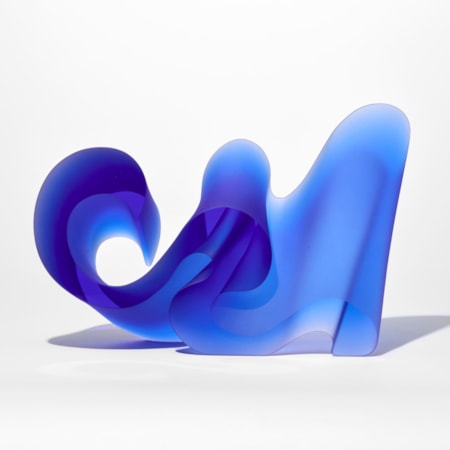 intense semi transparent blue prone curling and undulating standing form with a flat front and back hand made from glass