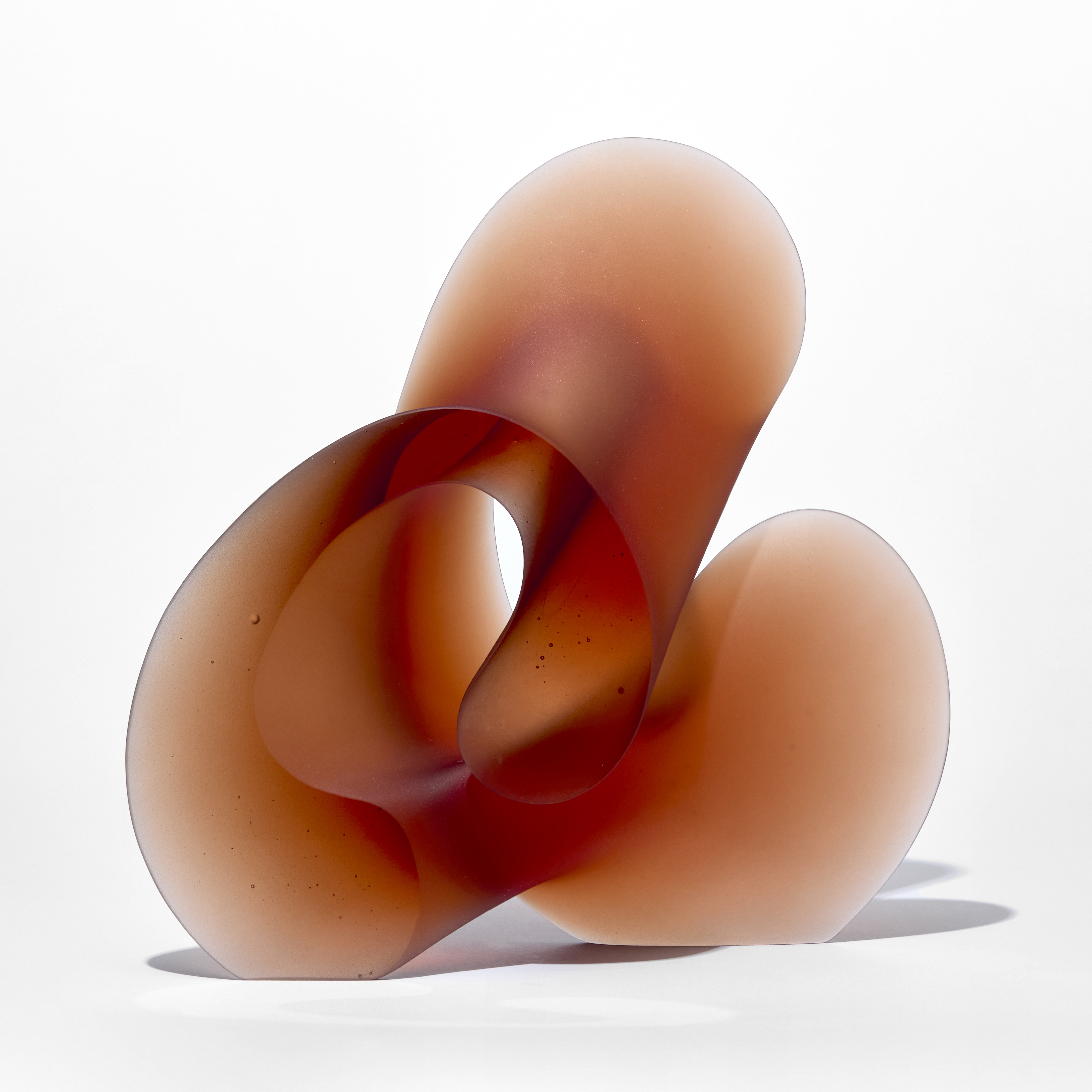 standing burnt orange red standing curling form with flat front and back with the other edge in three rounded sections hand made from glass