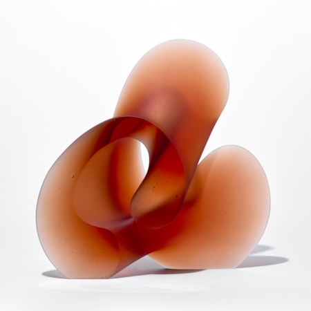 standing burnt orange red standing curling form with flat front and back with the other edge in three rounded sections hand made from glass