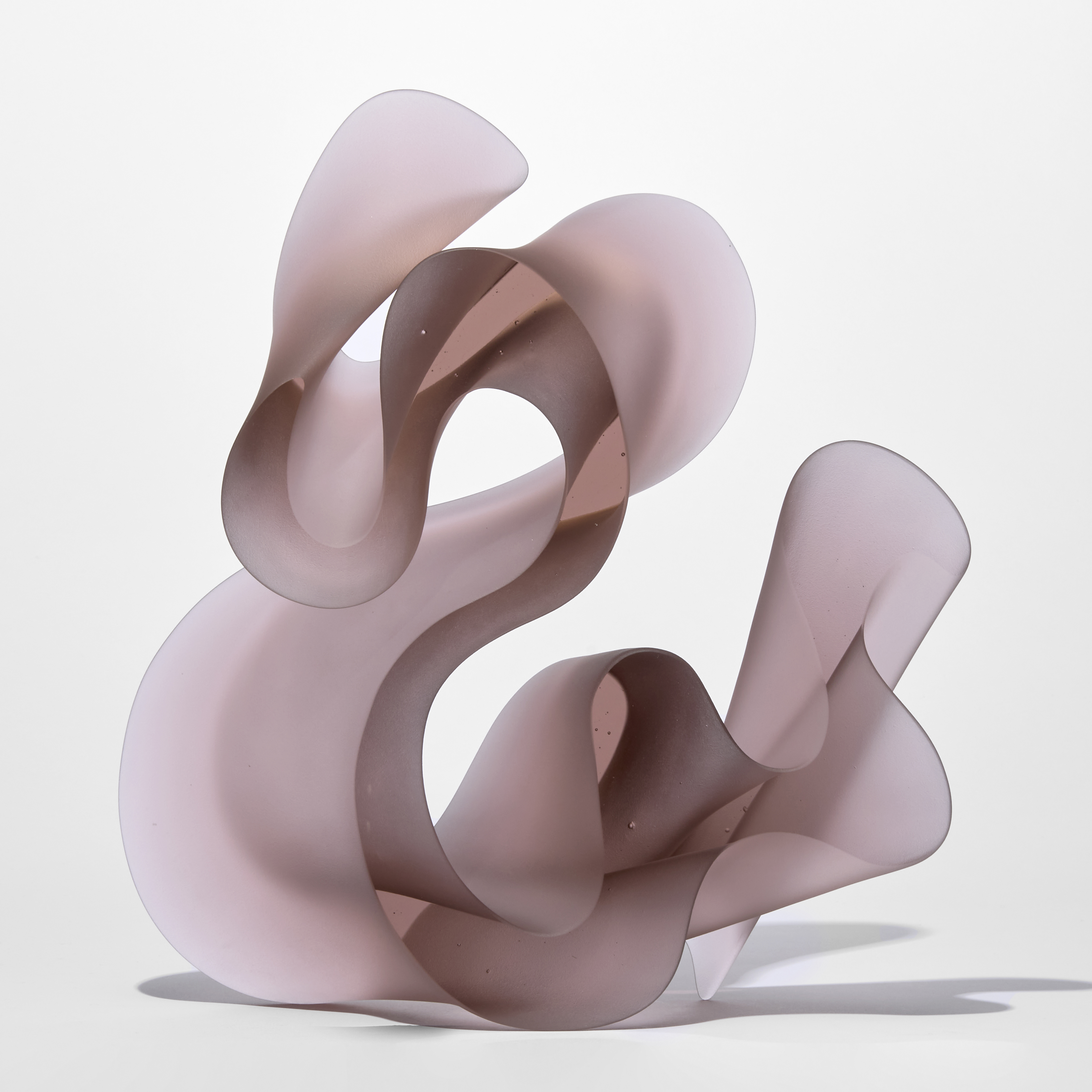 standing undulating semi transparent three dimensional standing form in soft rose pink with the appearance of a calligraphy flourish hand made from glass