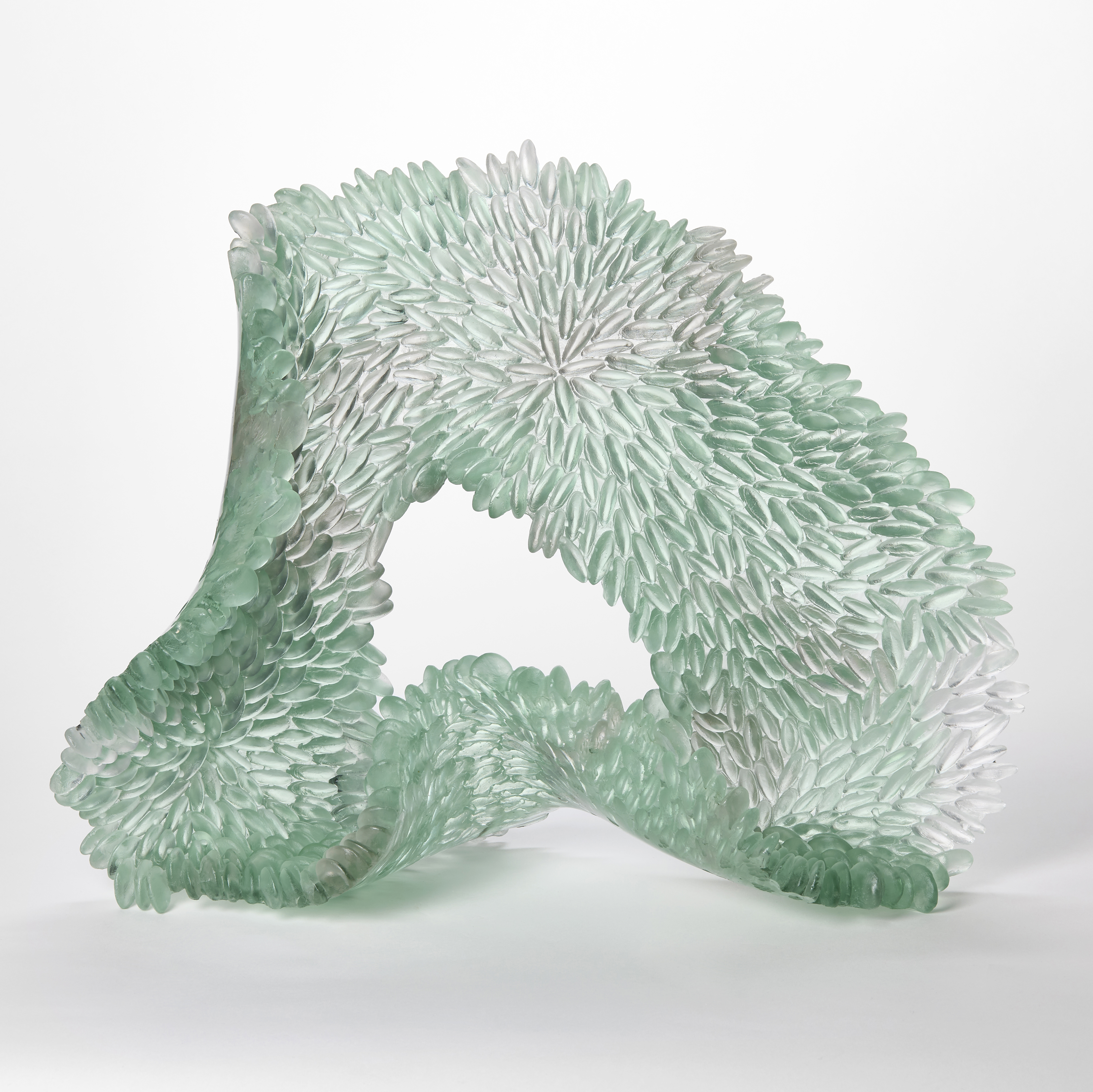 standing organic and softly shaped undulating ringed sculpture in semi transparent pale jade and grey with the front surface covered in raised scales hand made from glass
