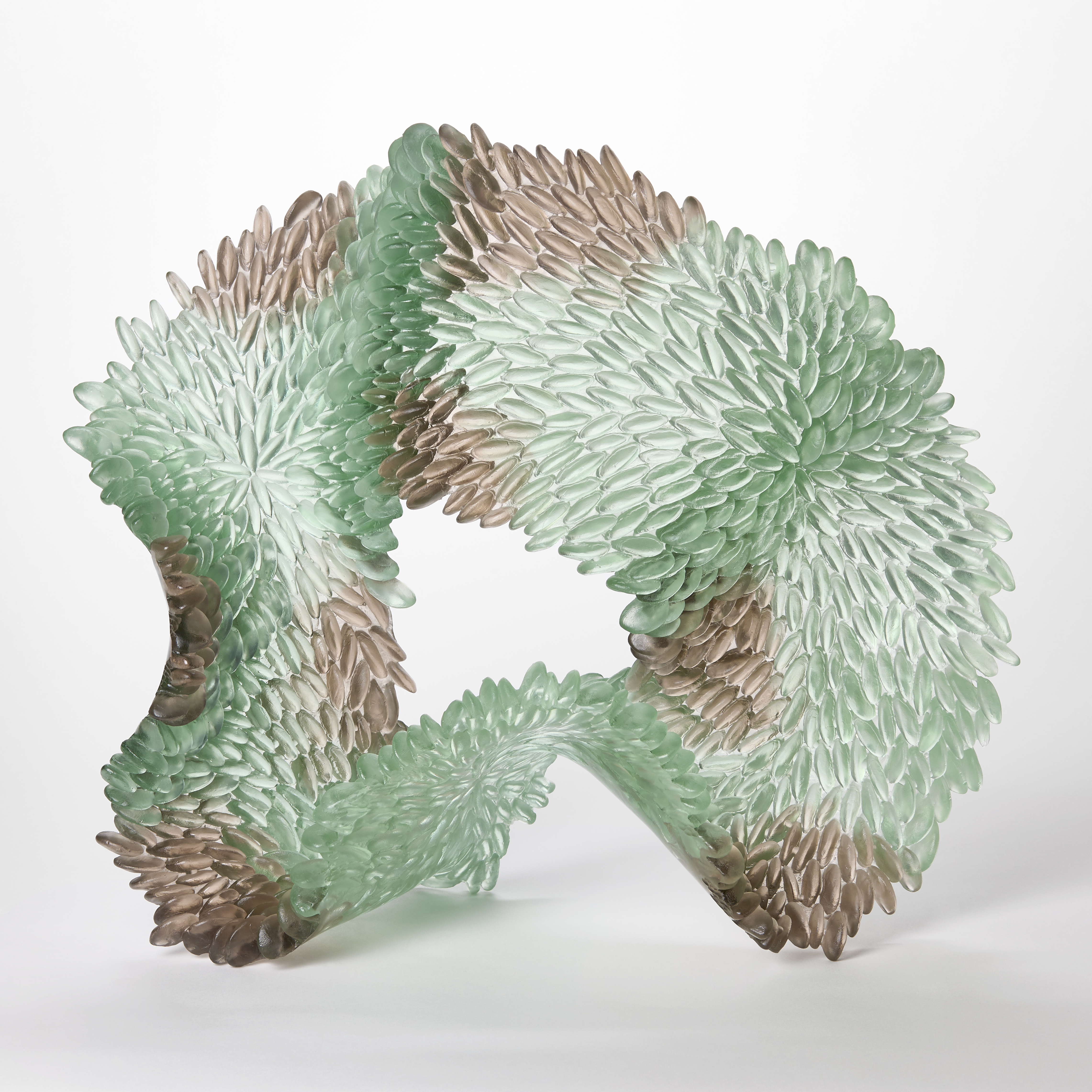 standing organically shaped undulating ringed sculpture with the front surface covered in raised ridged scales in semi transparent soft jade green and grey hand made from glass