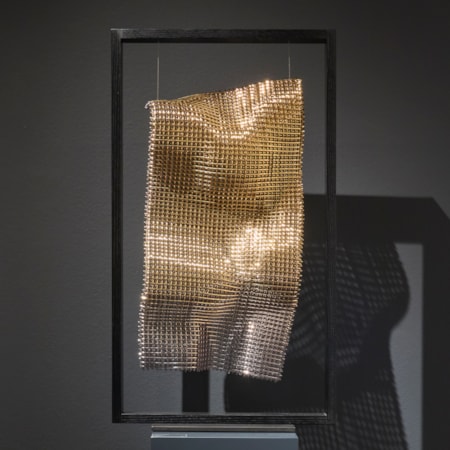 black wooden portrait standing rectangular frame holding a suspended undulating long sheet of cloth made from thick interwoven canes of glass with a gold finish