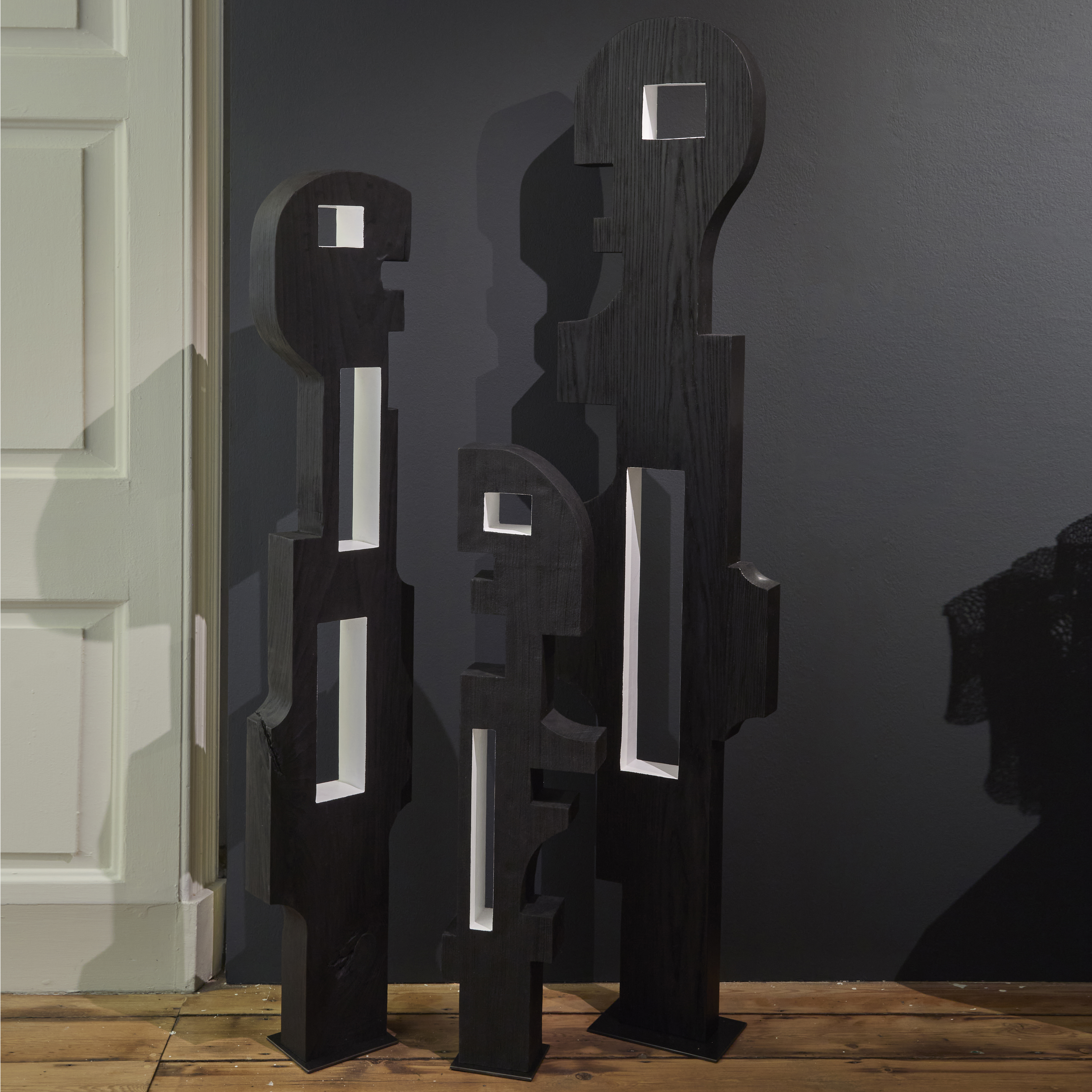 black wooden standing abstract figurative sculpture with cutout square and rectangular holes through the middle coloured white hand made and carved from ash