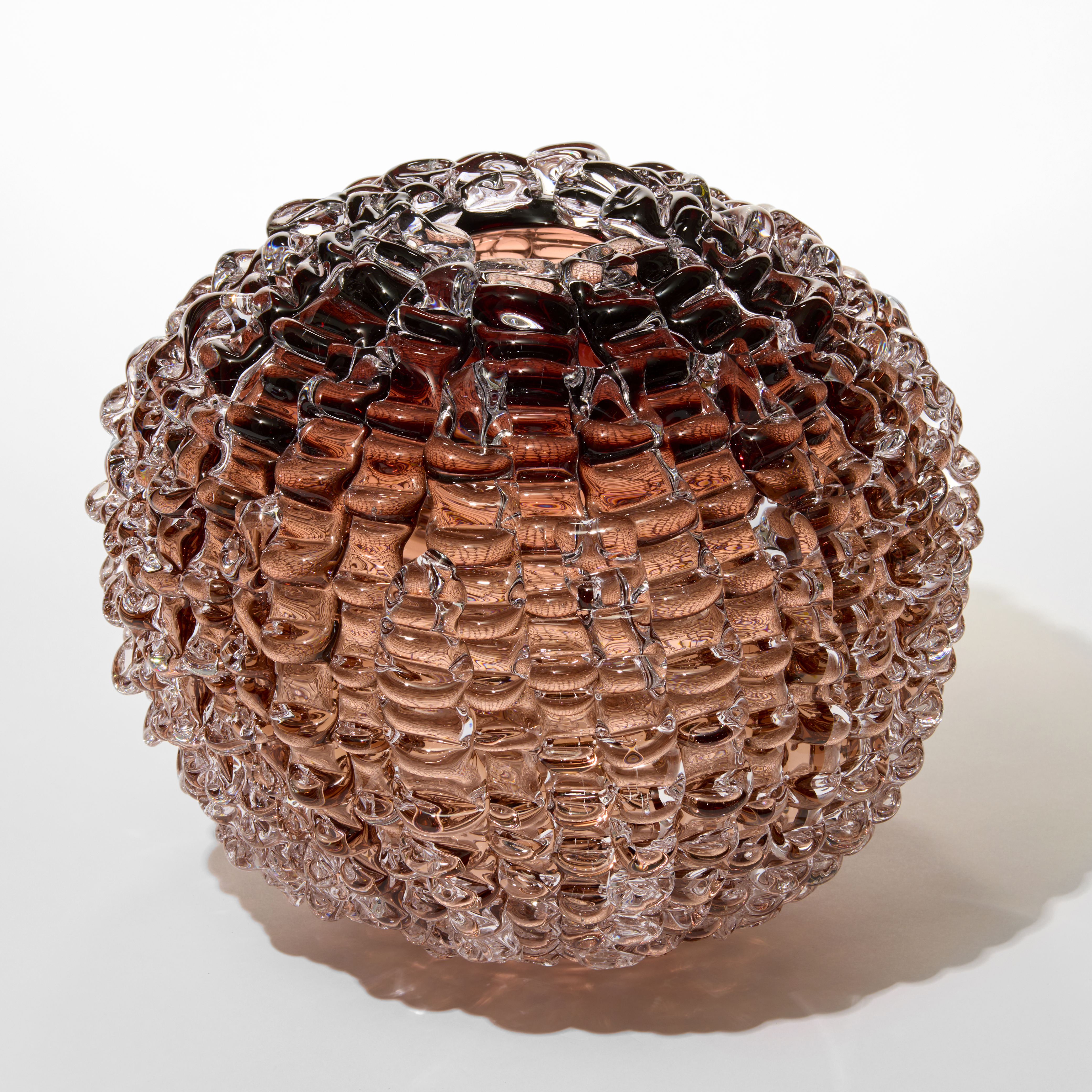 round ball shaped vase with a small top opening in transparent aubergine dusky pink with the outer surface covered in undulating ridged lines hand blown from glass