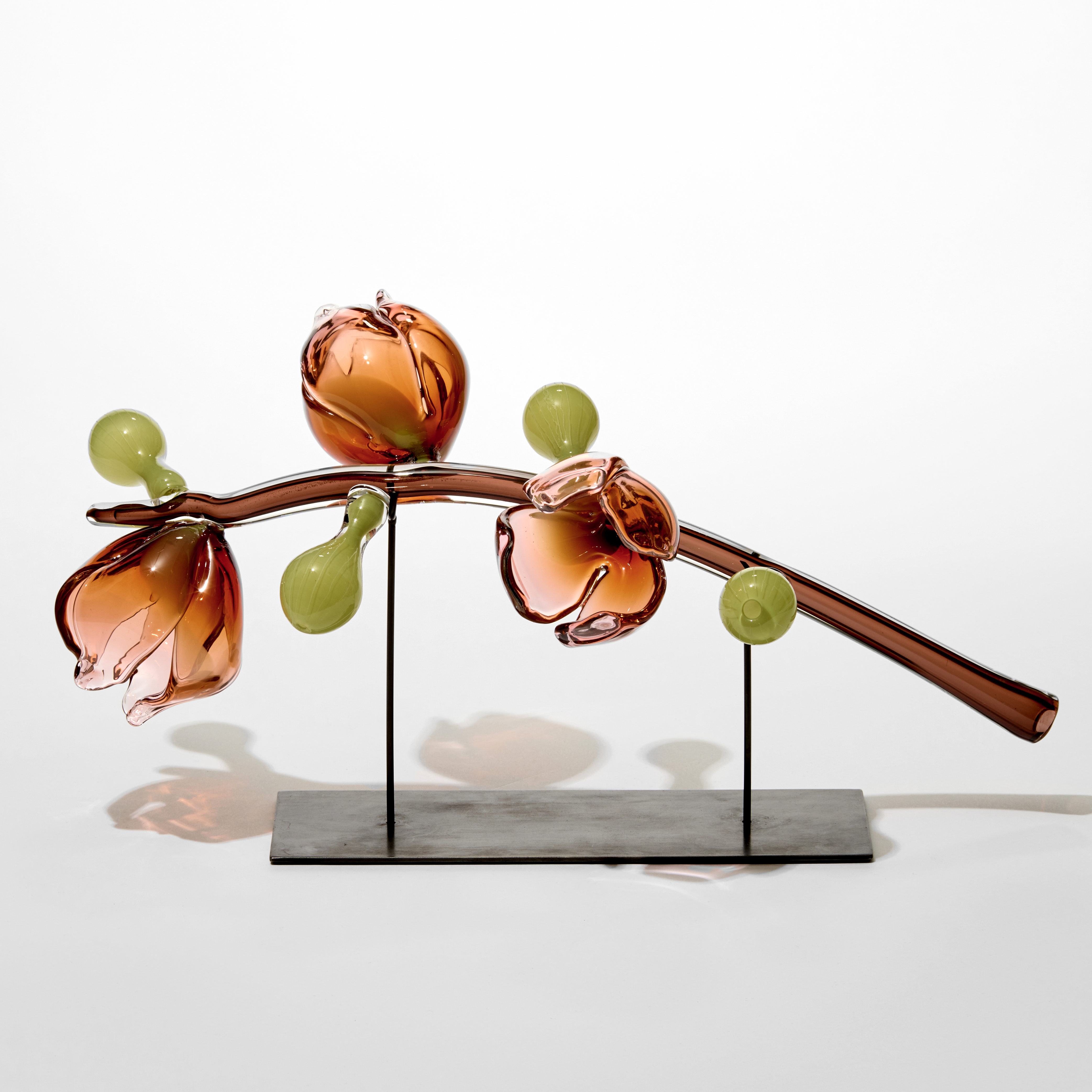 long transparent mid brown glossy stem with three soft peachy rose coloured abstract flowers and four green bulbous pods attached hand made from glass