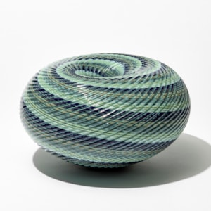 shiny ridged low round maelstrom whirlpool inspired sculpture consisting of thin spiralling bands of jade celadon blue grey and indigo handblown and cut from glass