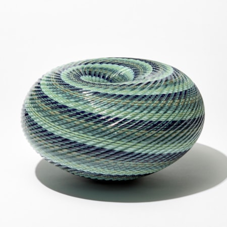 shiny ridged low round maelstrom whirlpool inspired sculpture consisting of thin spiralling bands of jade celadon blue grey and indigo handblown and cut from glass
