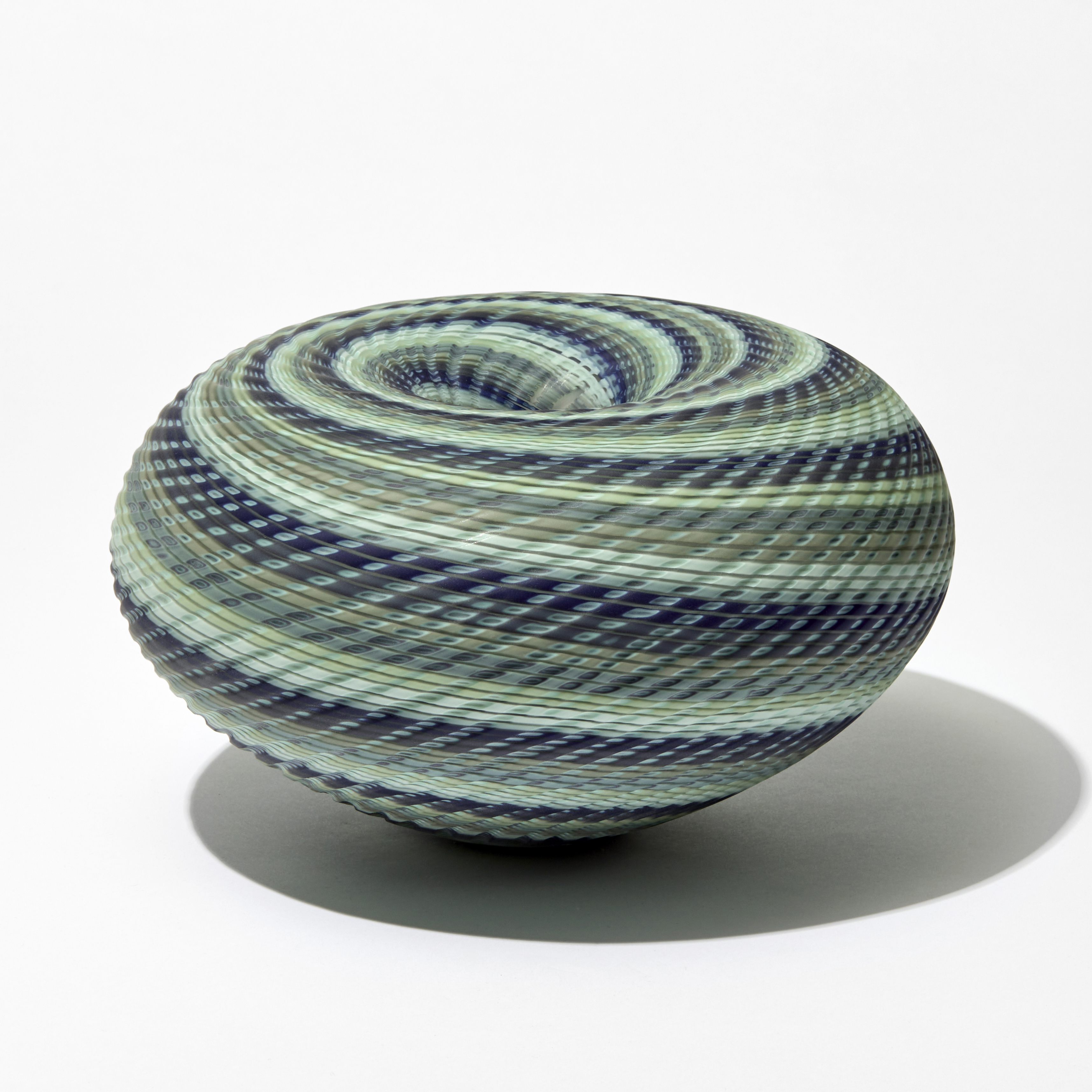 matt squat round donut shaped vessel with central descending inwards hole in coloured spiralling bands in celadon blue khaki and indigo handmade from blown and cut glass