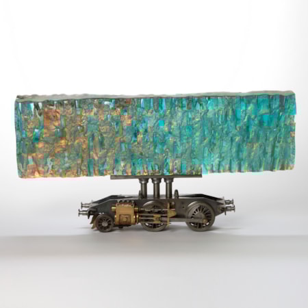 hand made cast glass large thick chunky textured long transparent horizontal block in iridescent colours of pinks peaches turquoises held aloft on a steel model rail way locomotive chassis