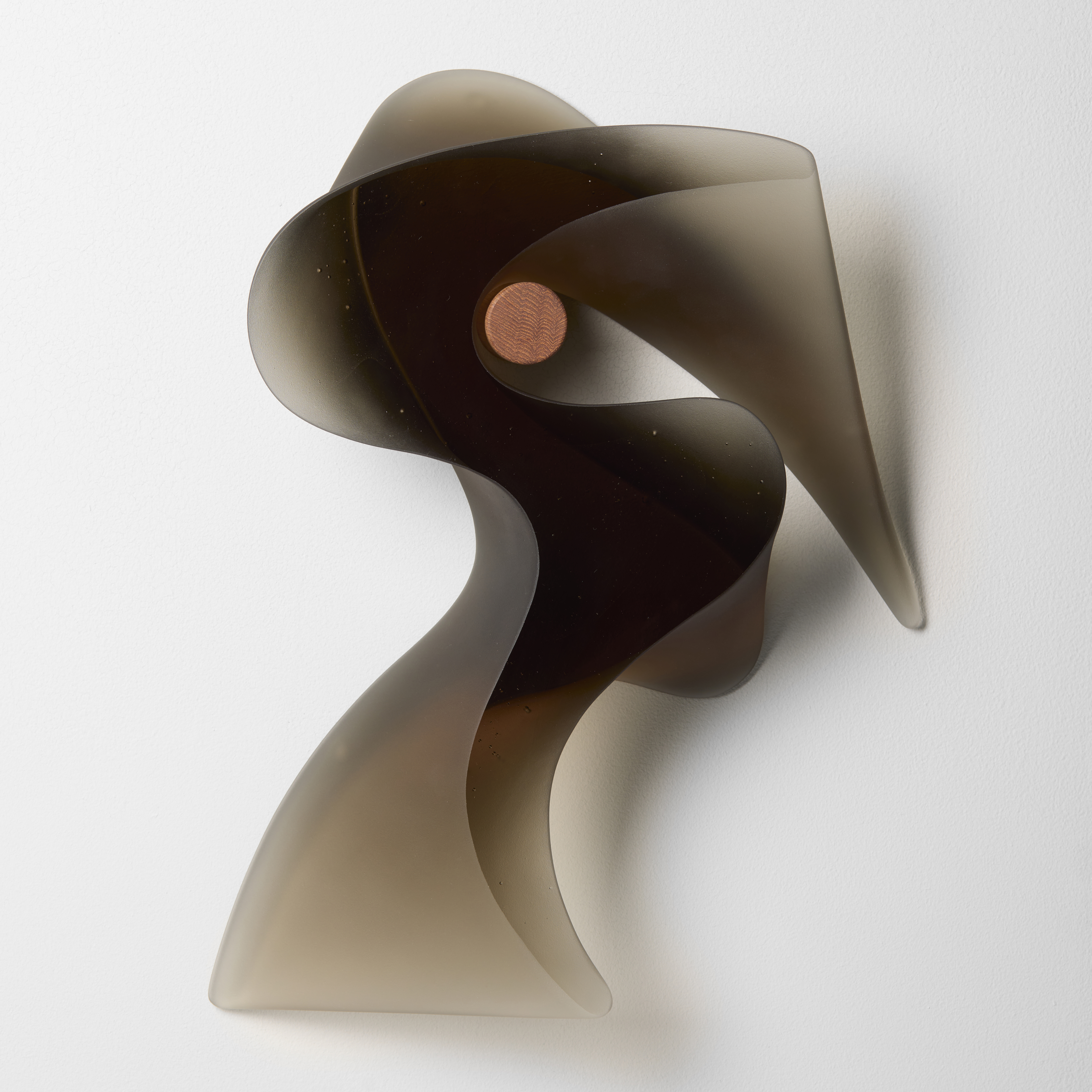 dark semi transparent bronze brown abstract sculpture with appearance of a flourish of calligraphy with a shiny front and back and frosted meandering side hand made from glass suspended on a chunky teak peg