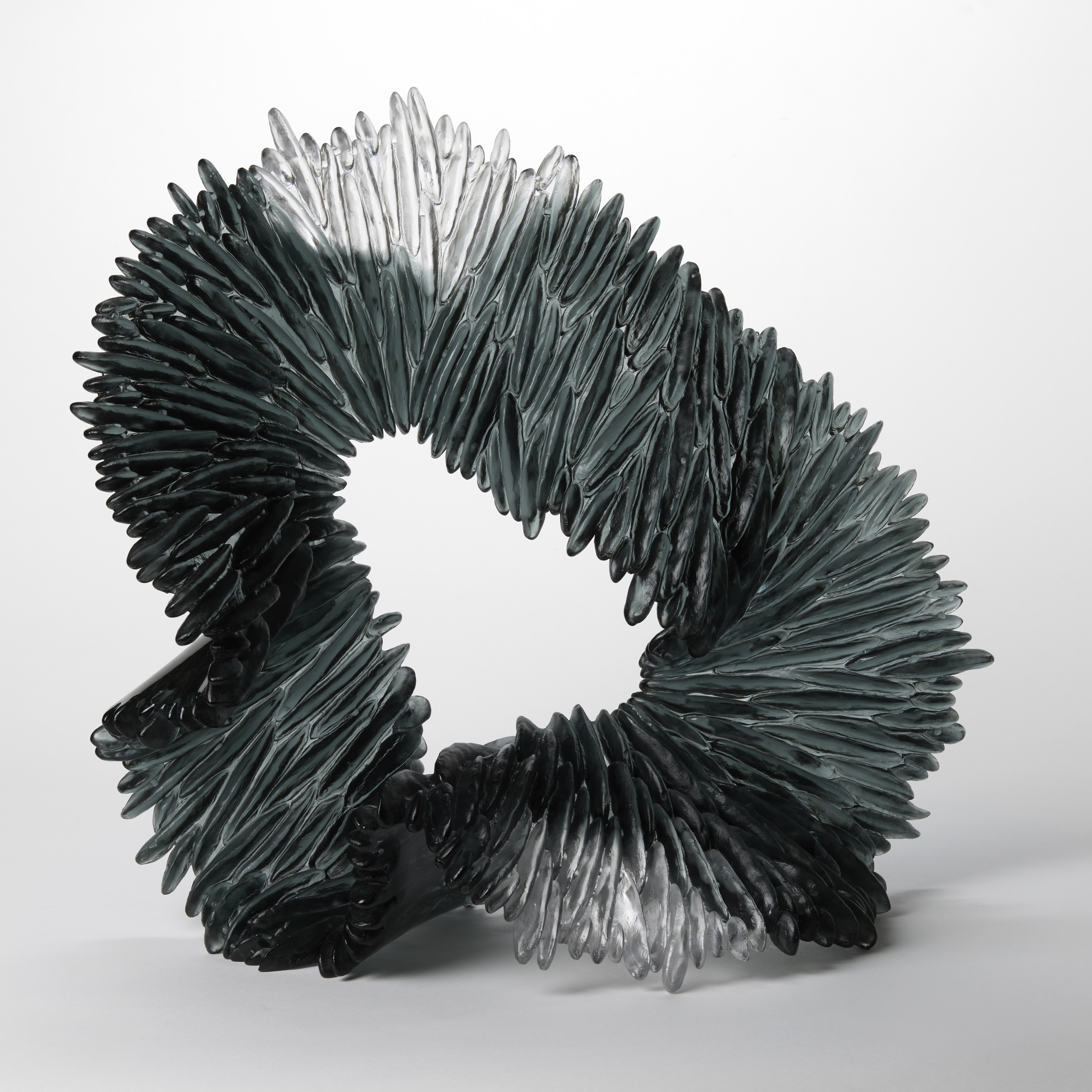 standing softly looped undulating ridged organic sculpture with the appearance stone in transparent grey and clear hand made from cast glass