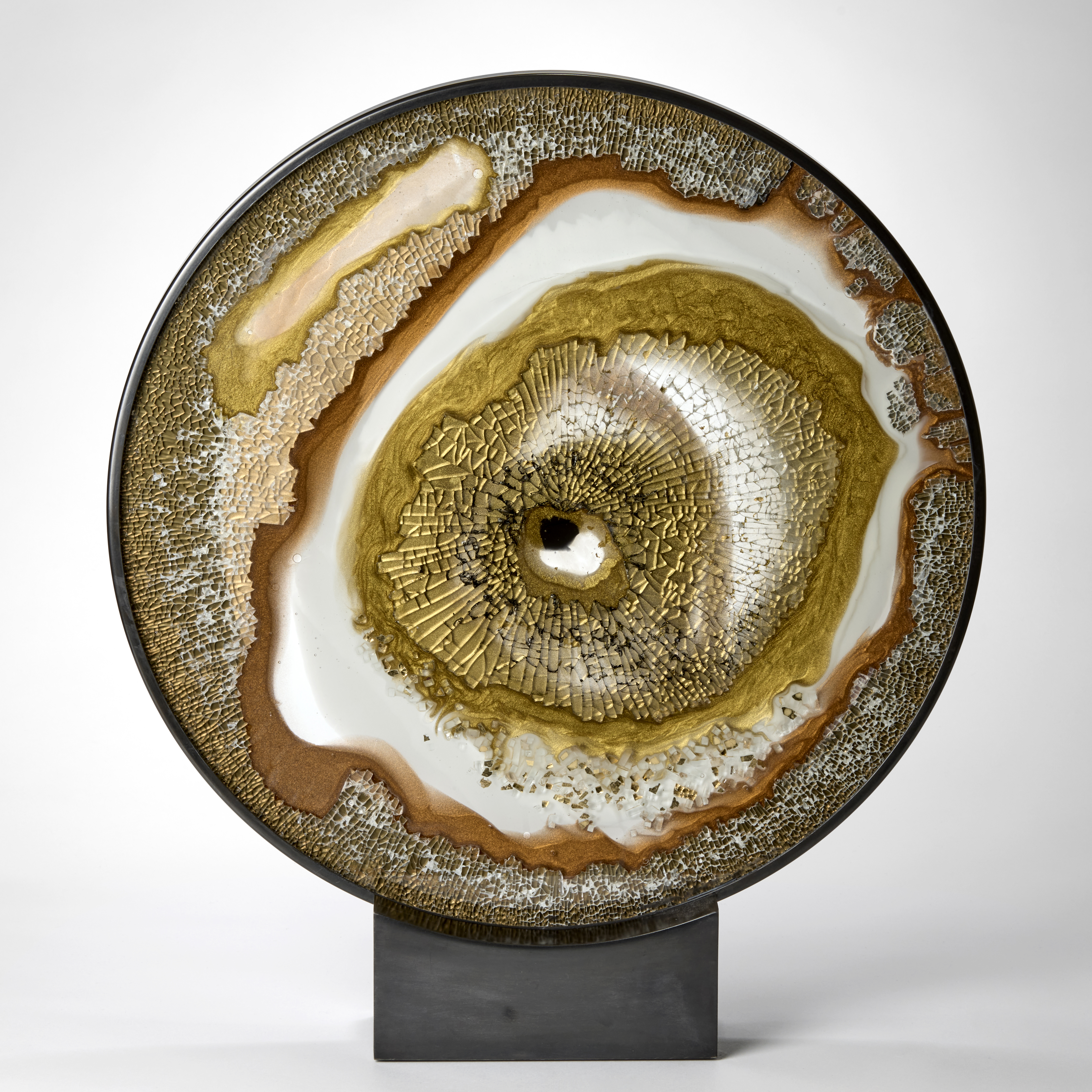 round dark metal frame holding disc shaped planes of shattered glass with abstract patterns in gold white and black on a pewter coloured low rectangular solid box base hand made from glass and steel