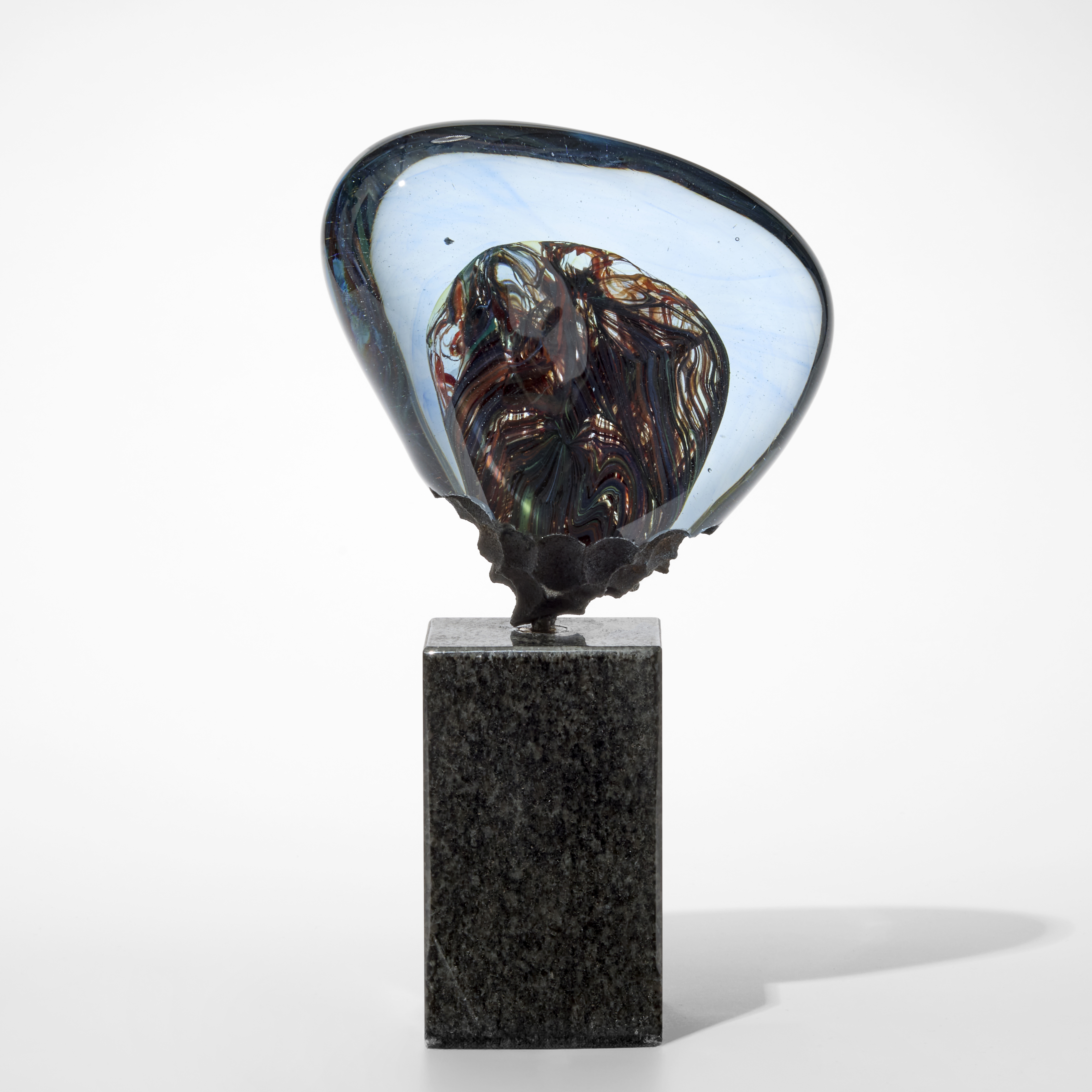 soft transparent inverted triangular glass mass in light steel blue with an intense interwoven mixed colour core perched upon a tall square granite base 