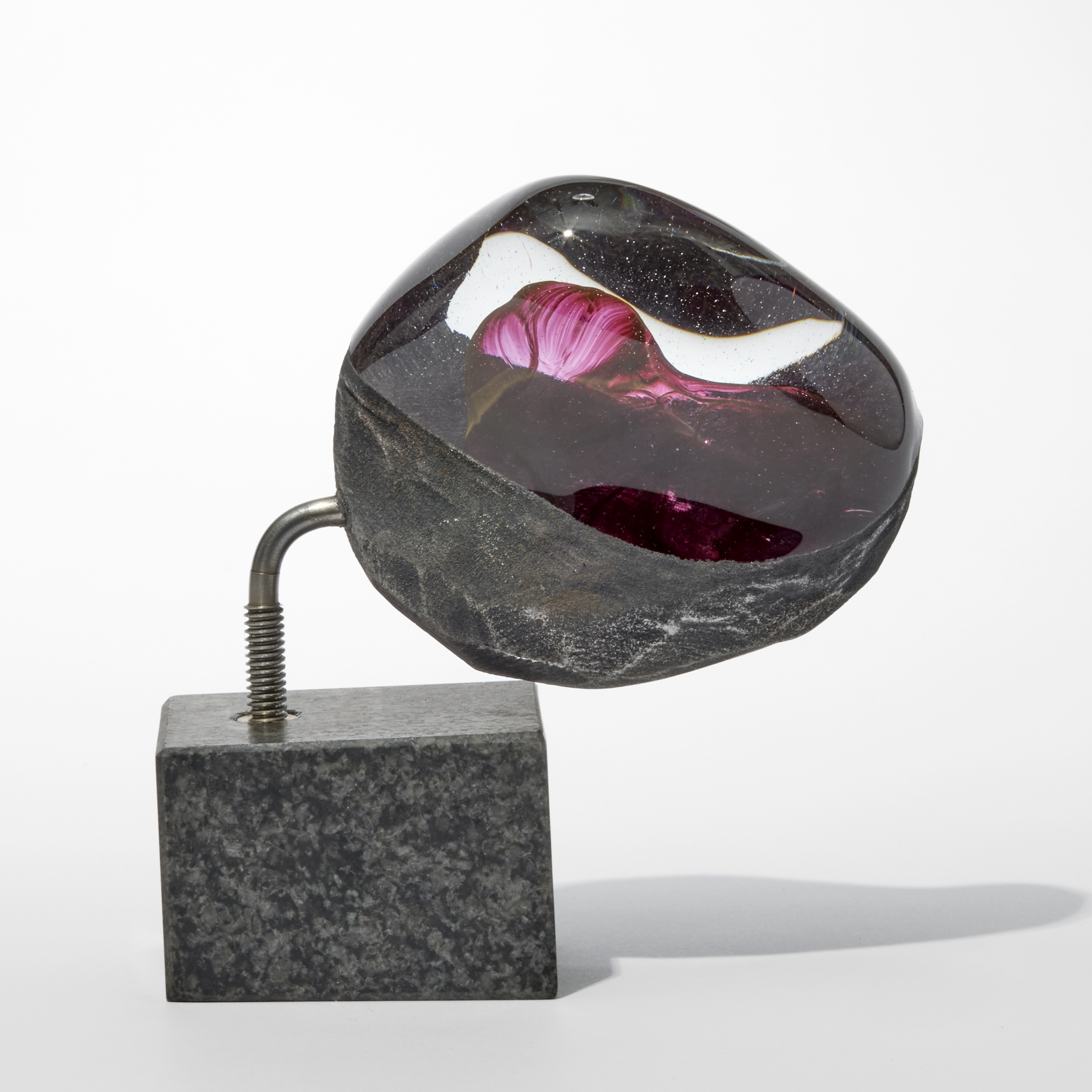 semi smooth and transparent glassrocky mass with a coarse underside and a red bulging mass trapped inside perched offset on an slab of granite