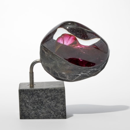 semi smooth and transparent glassrocky mass with a coarse underside and a red bulging mass trapped inside perched offset on an slab of granite
