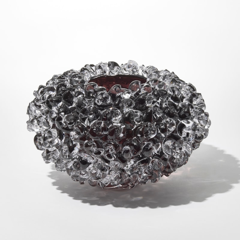 low round discus shaped transparent vase in clear and dark aubergine with the outside covered in raised twisted knotted sections hand made from blown and sculpted glass