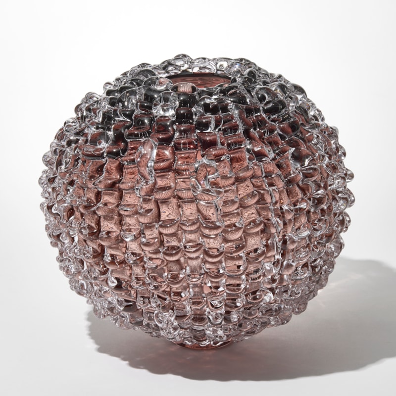 transparent round smokey aubergine tinted vase with small top opening and outer surface covered in soft merging linear lines with raised ridges hand made from blown and sculpted glass