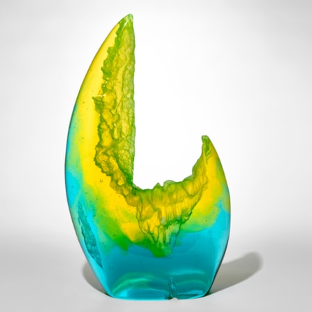 standing transparent rock like form with one side towering higher than the other side in a crab claw like form with bright turquoise at the base merging to lime green and then efflorescent yellow hand made from cast glass