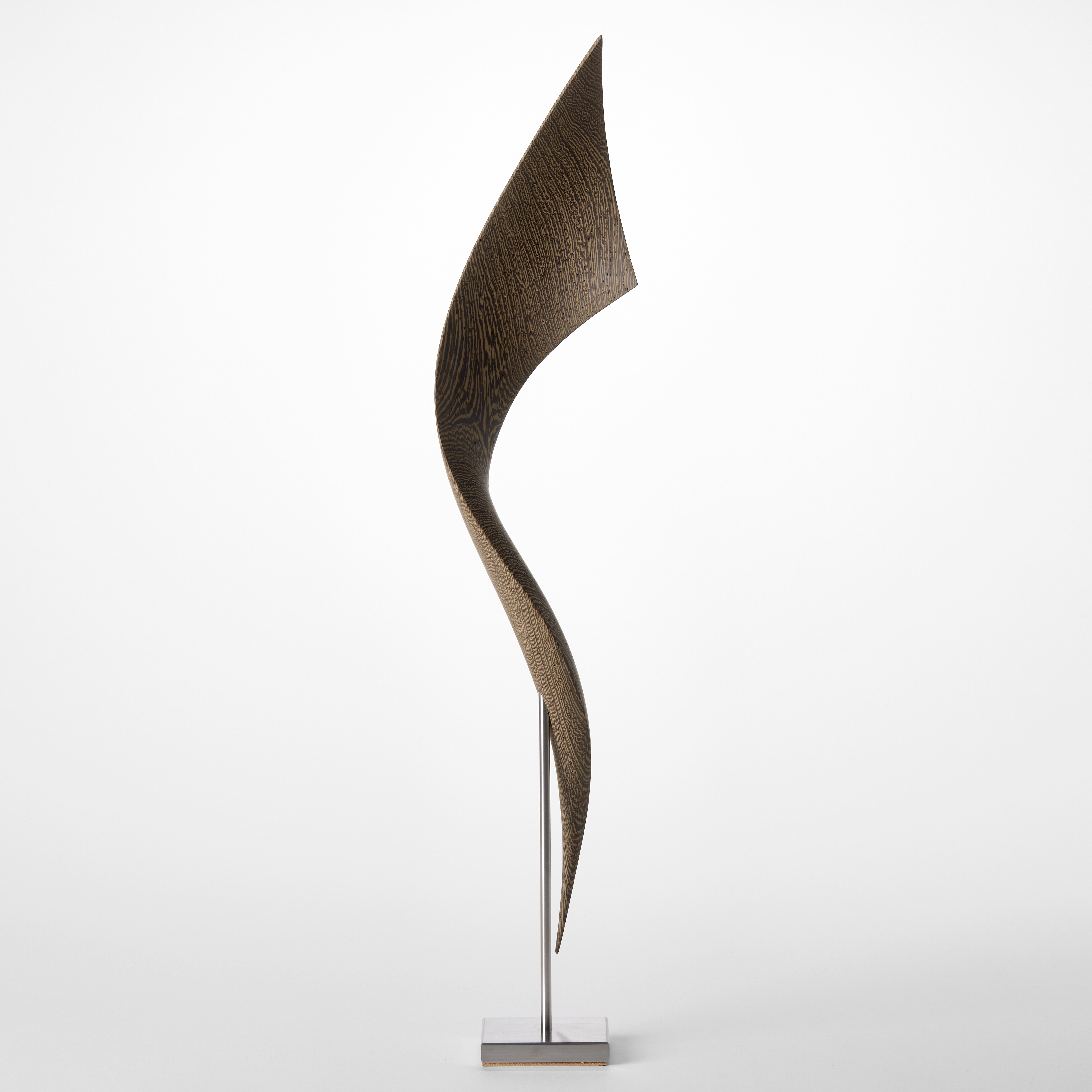 simple stainless steel base holding above a tall winding and widening ribbon of curing wood hand sculpted from wenge 