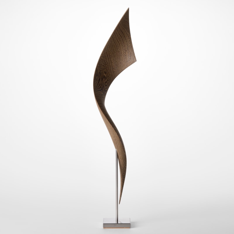 simple stainless steel base holding above a tall winding and widening ribbon of curing wood hand sculpted from wenge