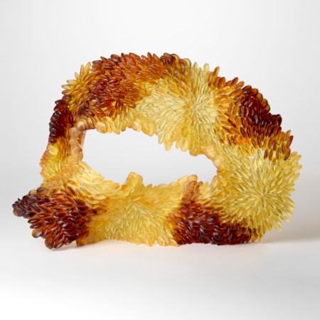 standing opaque organic edged oval form in yellow and dark amber with one side covered in raised tessellated scales hand made from cast glass