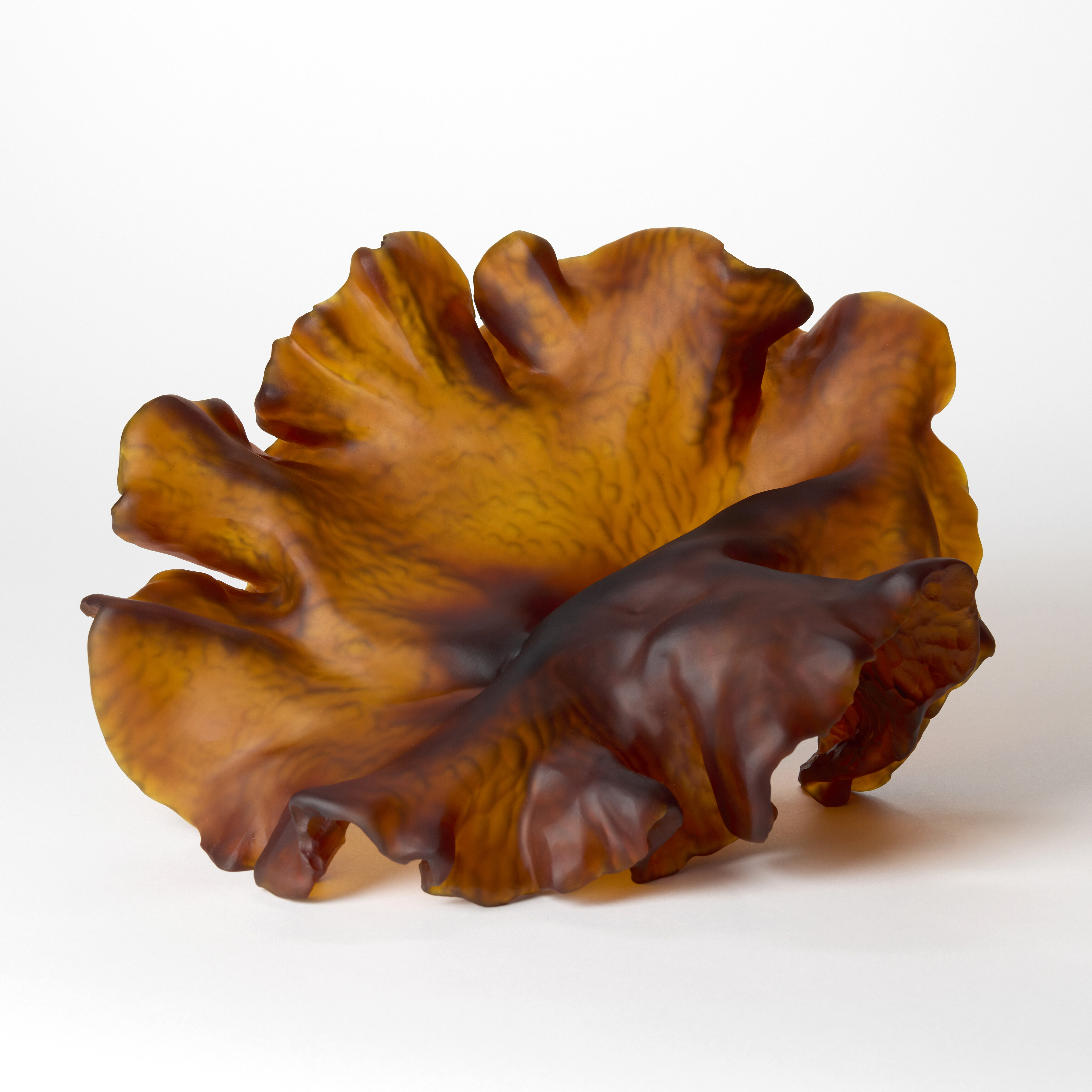 opaque dark amber organic form resembling a piece of round frilly seaweed hand made from cast glass with a ridged textured cut into the under surface