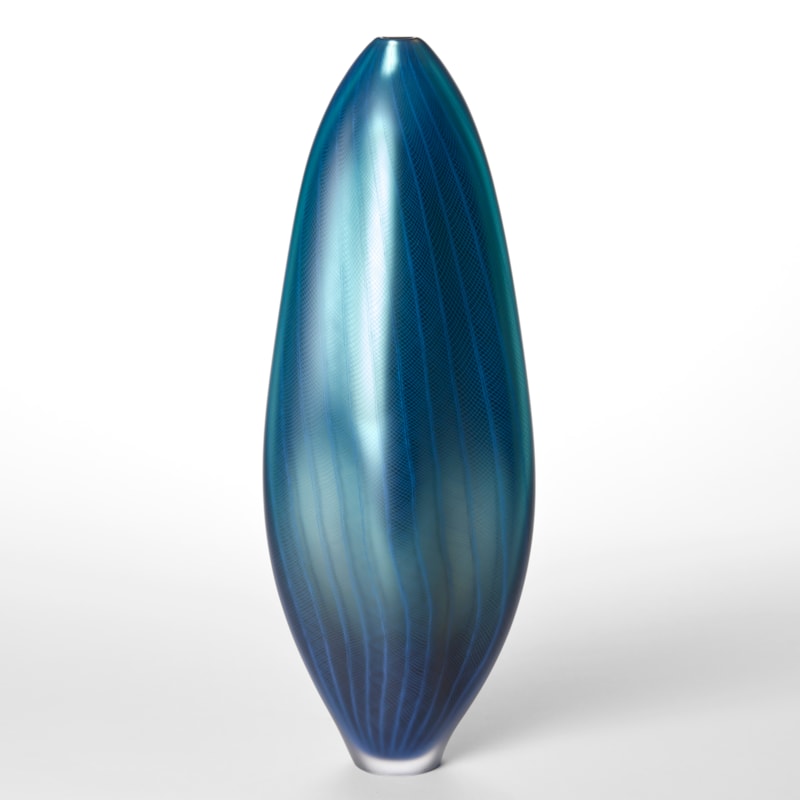 tall amorphic standing fluid form with small top opening and metallic satin surface in a mix of blue colours with a fine repeat lined pattern on the top hand made and blown from glass