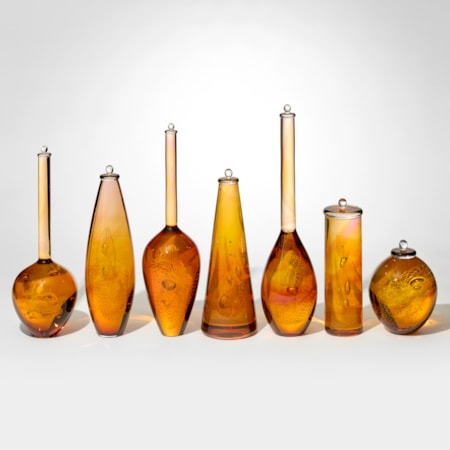series of seven amber gold and pink transparent bottles in differing shapes with bubbles and patterns trapped within each one hand made from glass