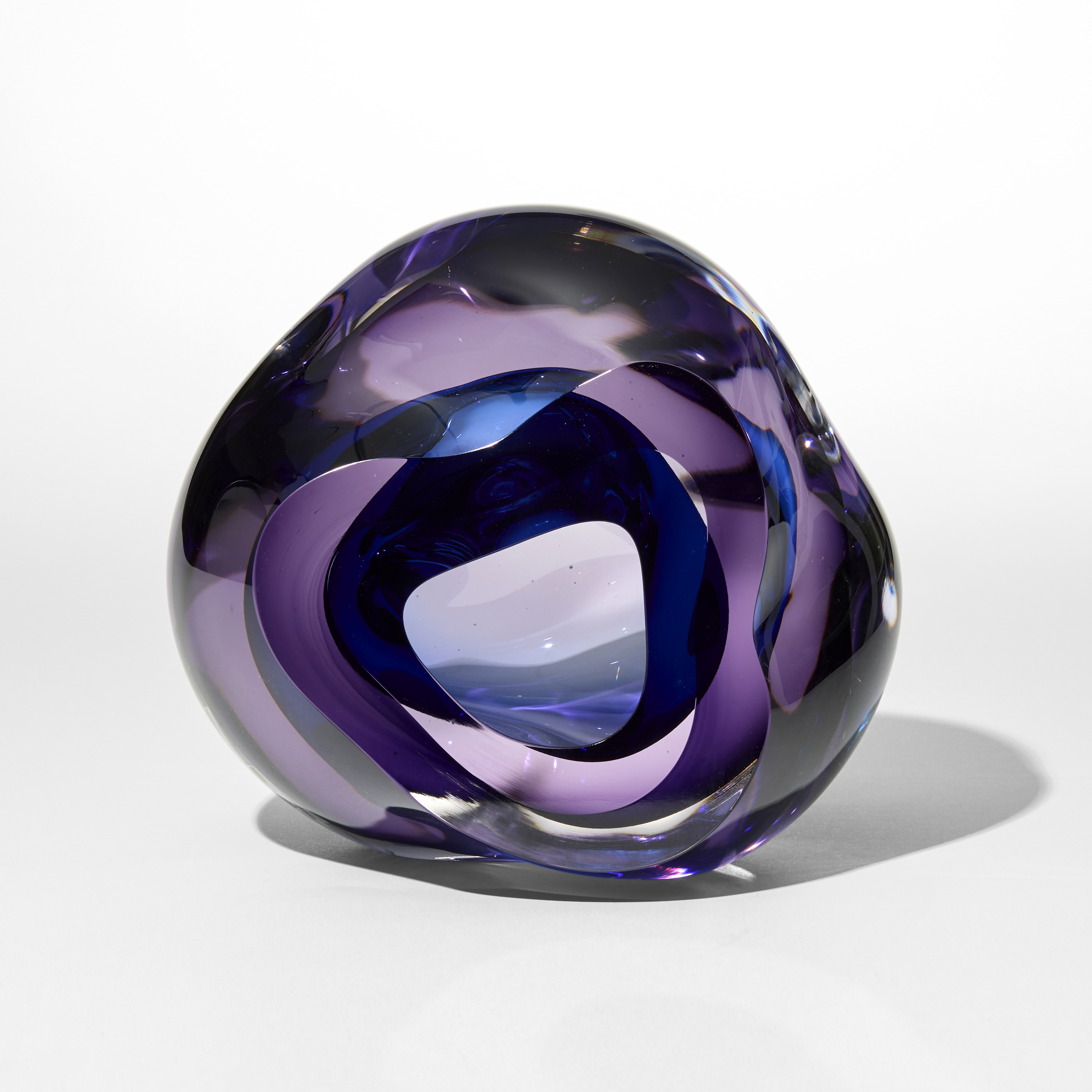 transparent soft amorphous pebble in layers of clear purple and rich blue with a central cavity with the opening from the front hand blown and sculpted from glass